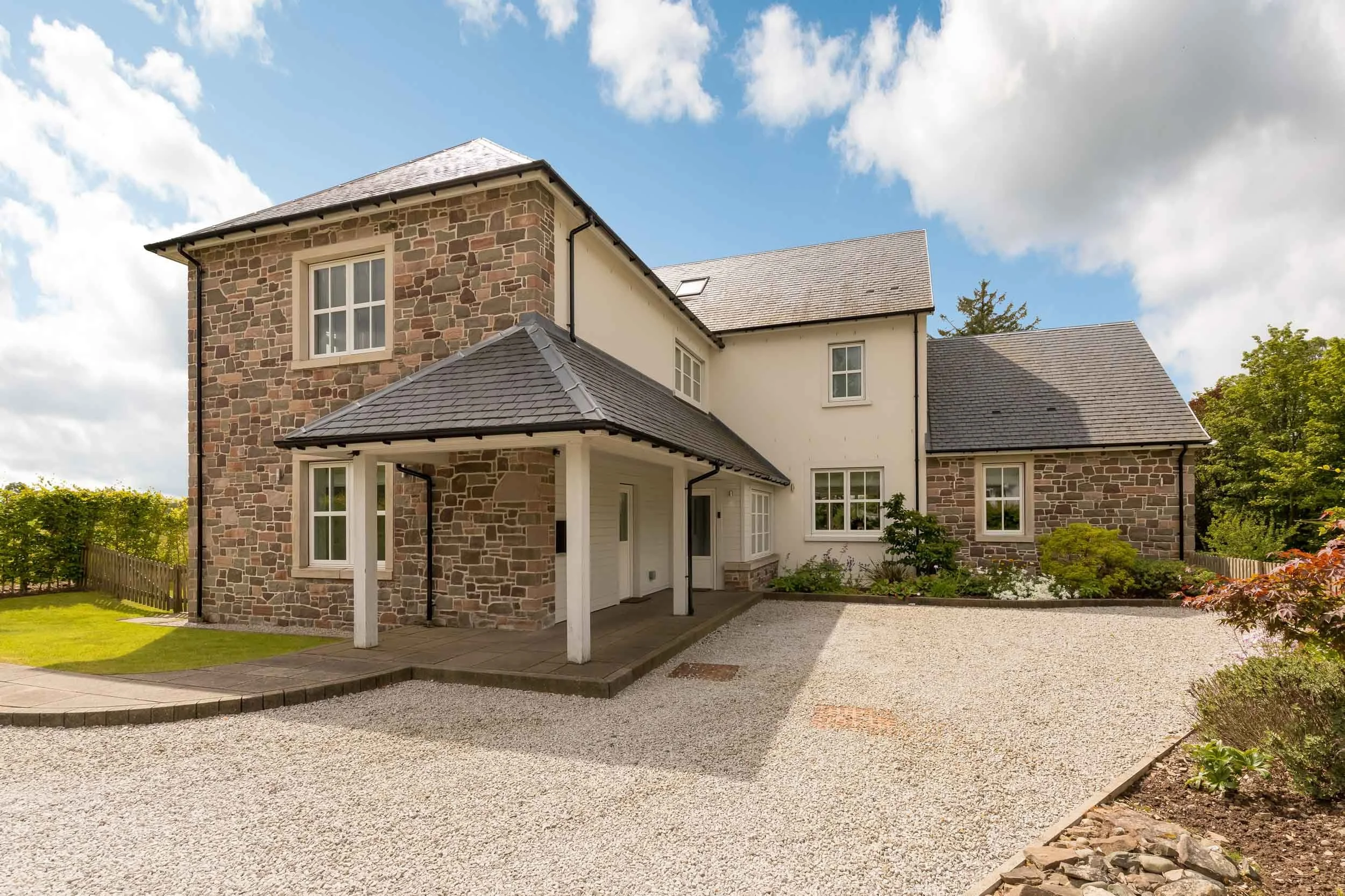 A two-story house with a mix of stone and white exterior walls, gray tiled roof, and a small porch area.