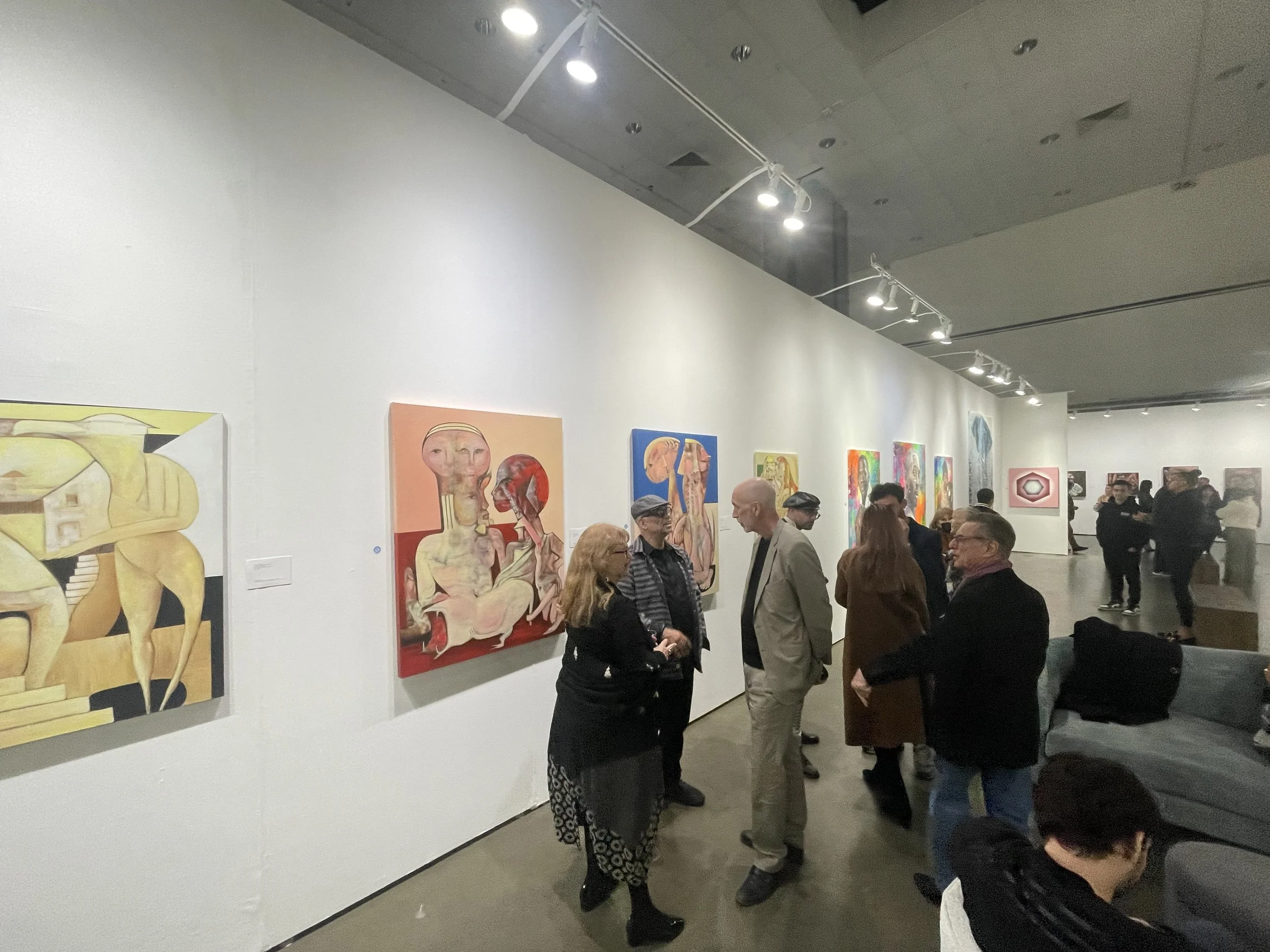 People viewing and discussing abstract and colorful modern artwork at an art gallery.