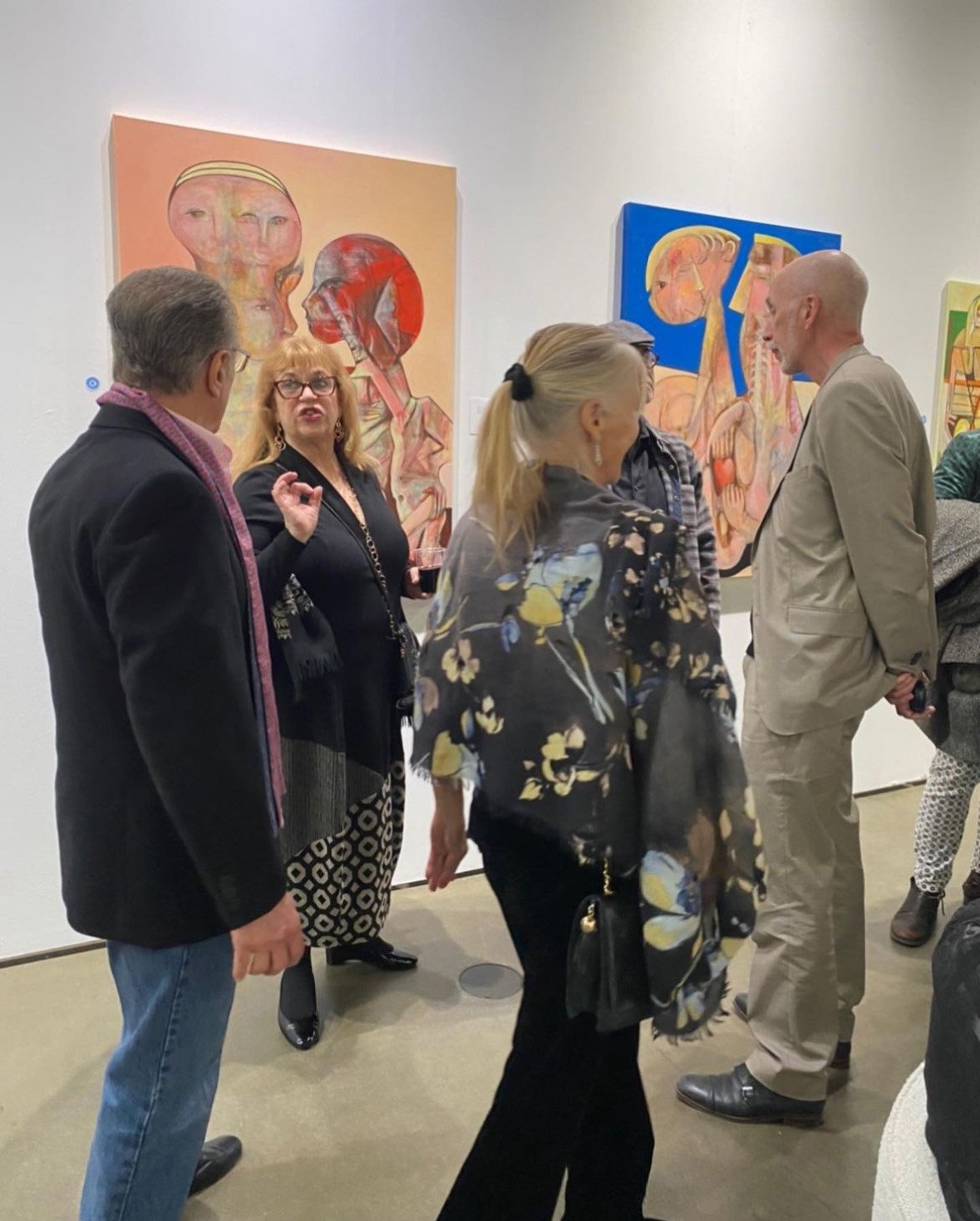 A group of people standing and talking in an art gallery with colorful abstract paintings on the wall.
