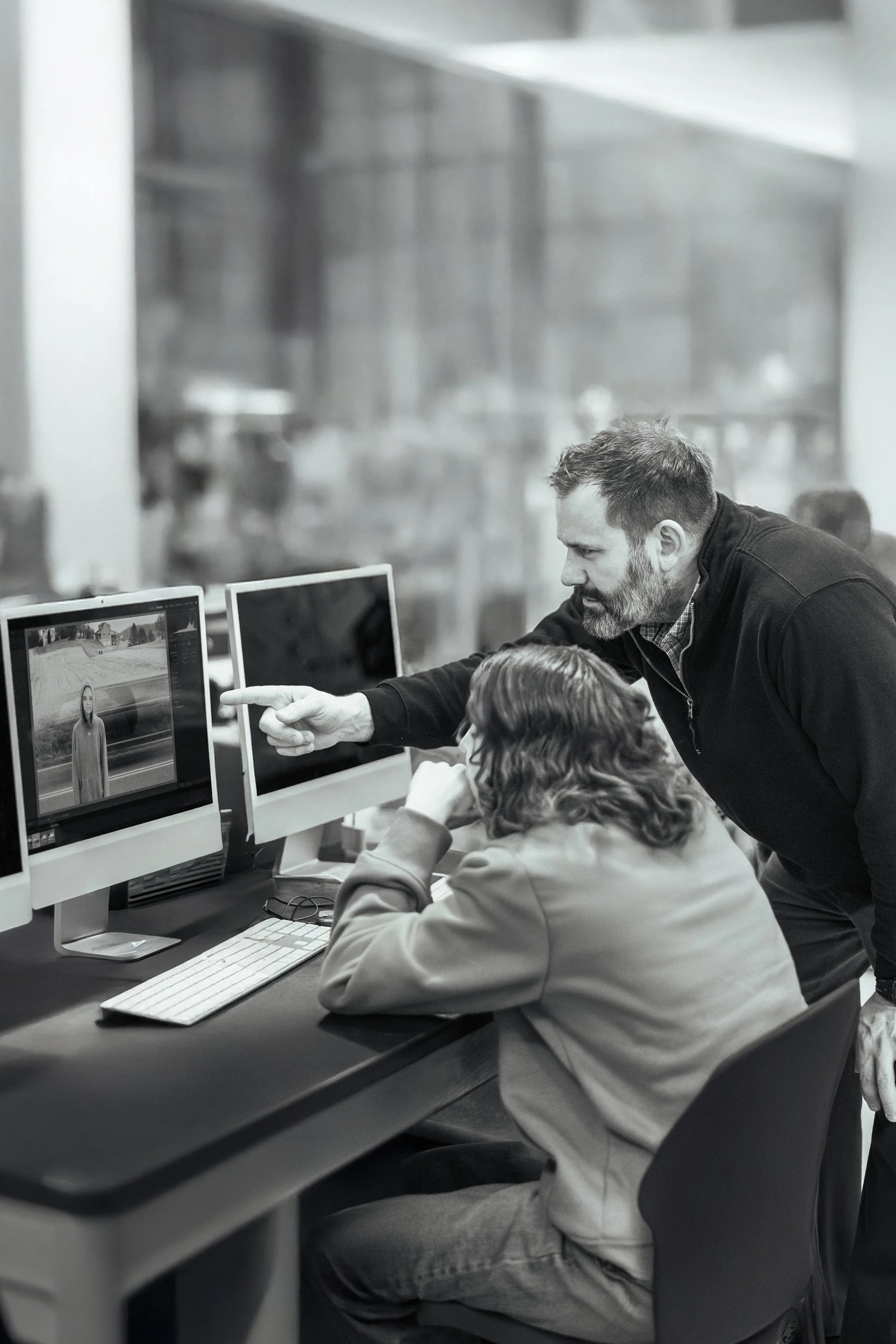 Man teaching woman about photo editing on a computer in a classroom or studio.
