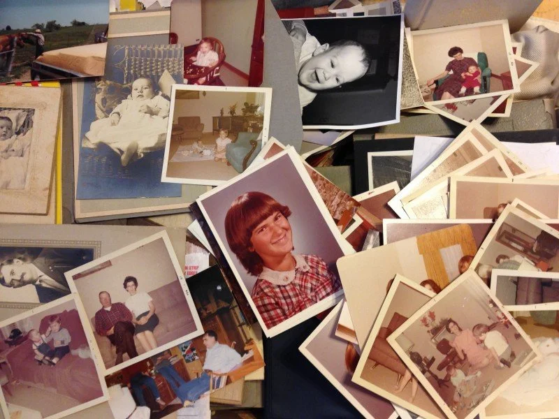 A collection of vintage photographs and printed family pictures scattered on a table.