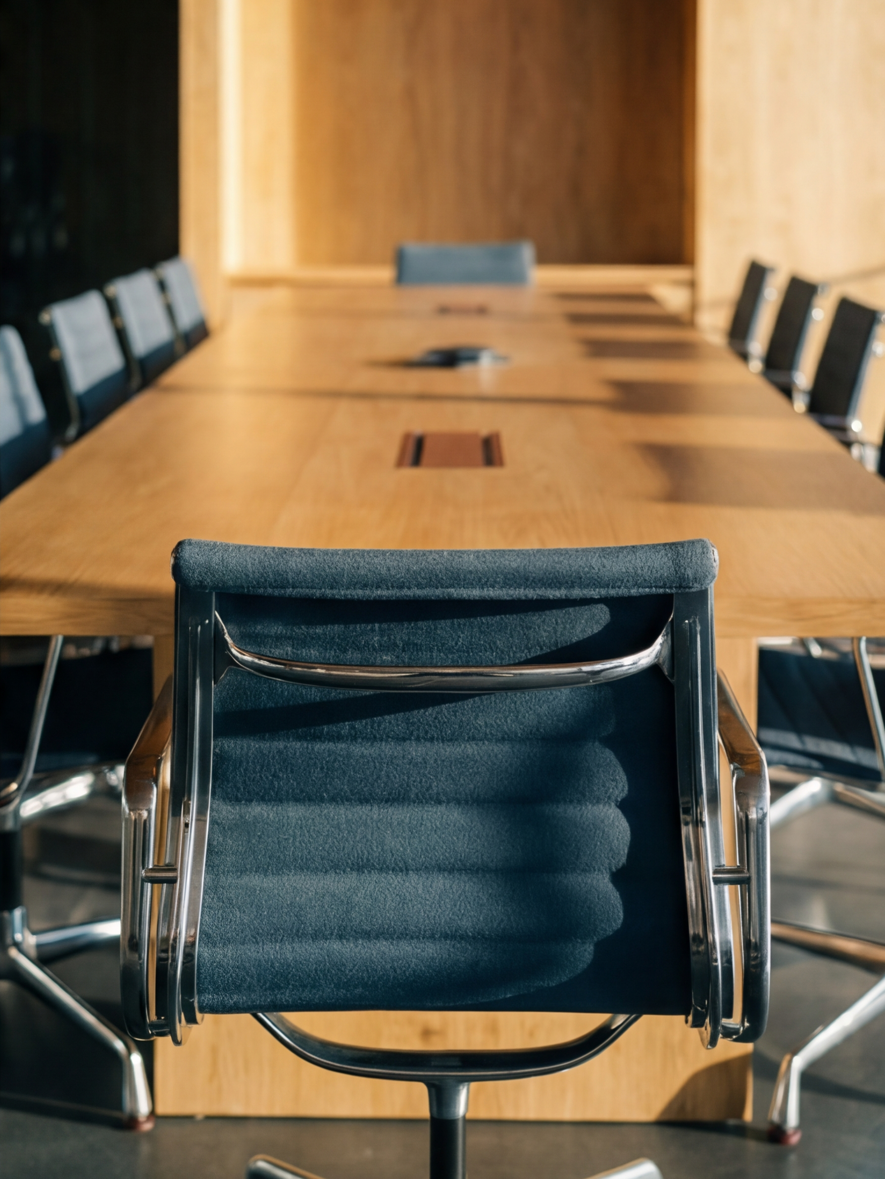 Empty conference room with a long wooden table and black office chairs.