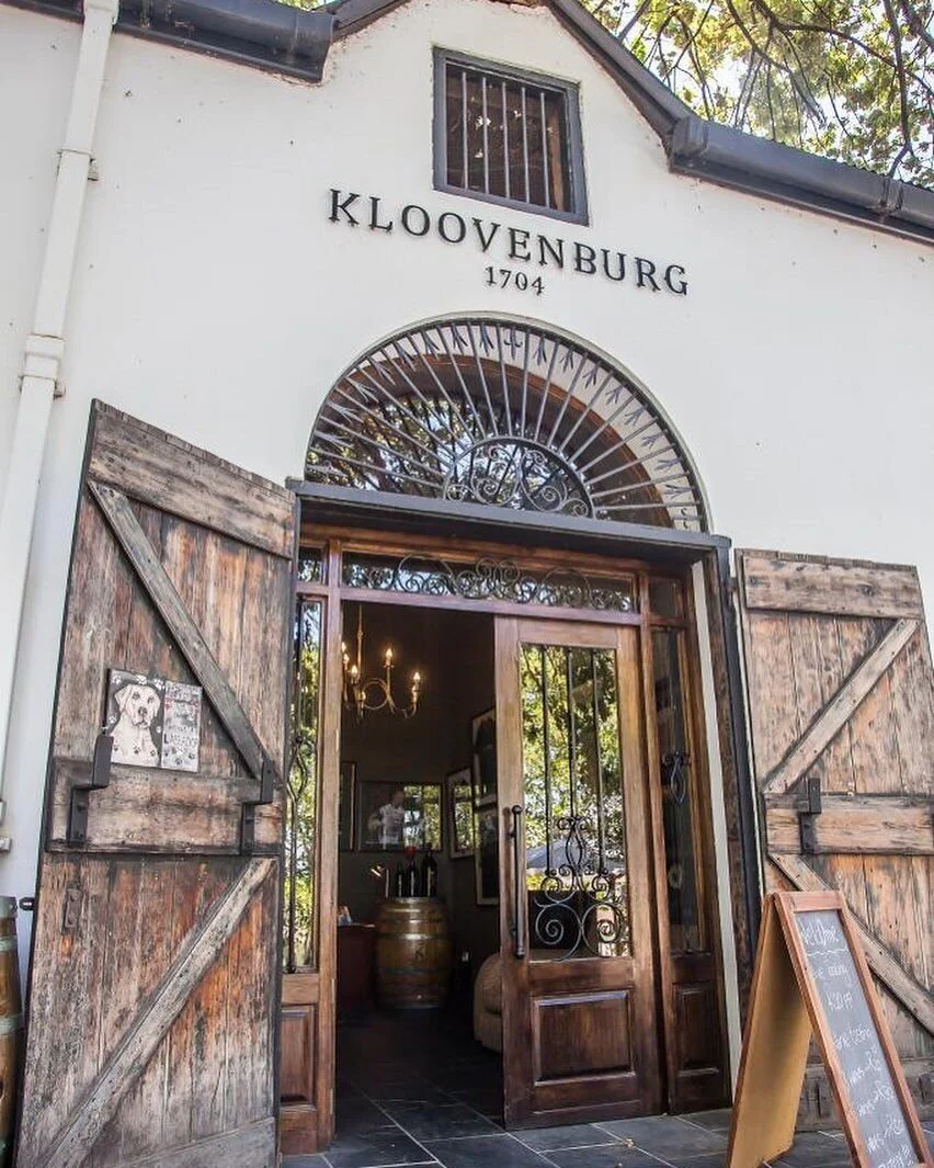 Entrance to Kloovenburg, a historic building from 1704, with wooden doors and decorative ironwork, and a sign showing this is a winery or similar establishment.
