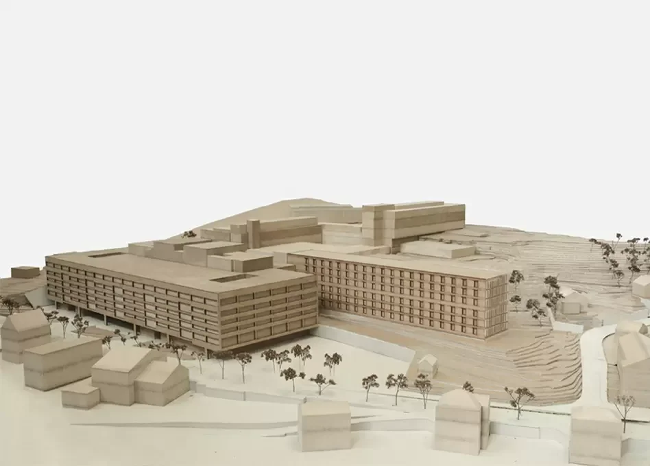 Architektenmodell eines großen Gebäudes mit mehreren Etagen, umgeben von kleinen Häusern und Bäumen, auf einem Modell eines Geländes.