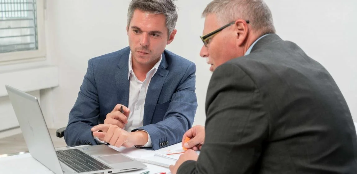 Zwei Männer in formeller Kleidung sprechen bei einem Meeting im Büro.