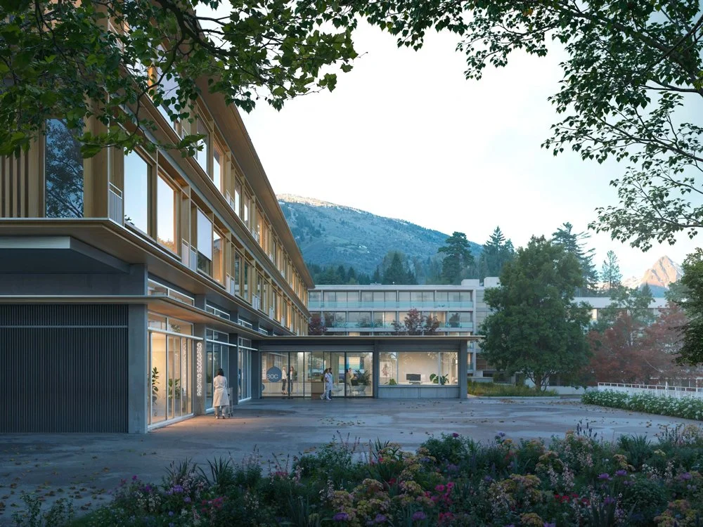 Moderates modernes Krankenhausgebäude mit Glasfassaden, umgeben von Bäumen und Bergen im Hintergrund, während Personen den Eingang betreten.
