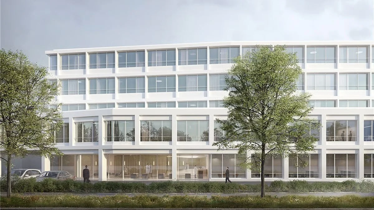 Ein modernes, vierstöckiges Bürogebäude mit großen Fenstern und begrüntem Vorplatz, Bäume im Vordergrund, einige Menschen und Autos vor dem Gebäude.