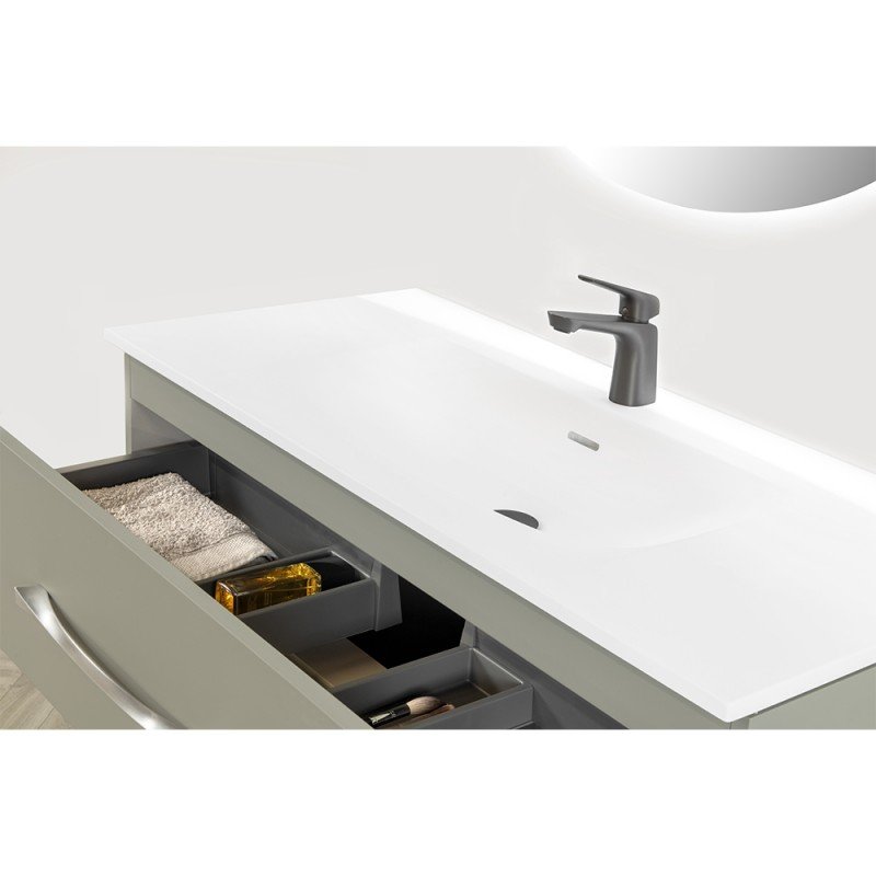 Meuble de salle de bain blanc avec un lavabo intégré et un miroir circulaire, tiroirs partiellement ouverts contenant des serviettes, un flacon de savon et des accessoires.