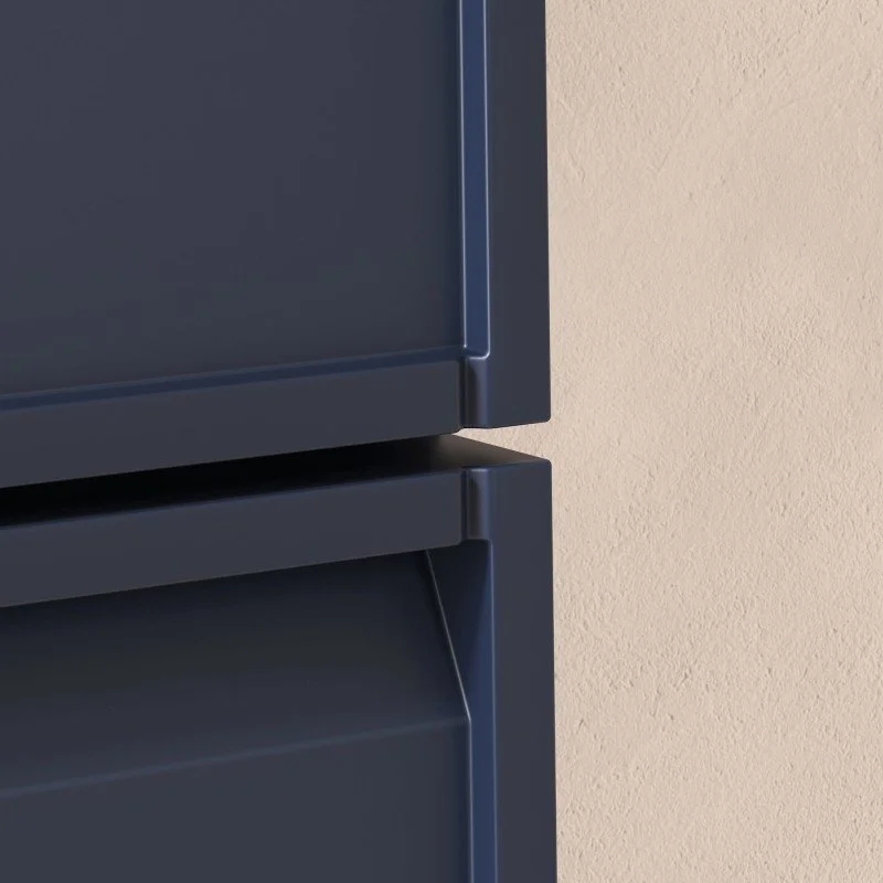 Zoom sur une partie de deux armoires métalliques empilées l'une sur l'autre, couleur gris foncé, avec un mur beige en arrière-plan.