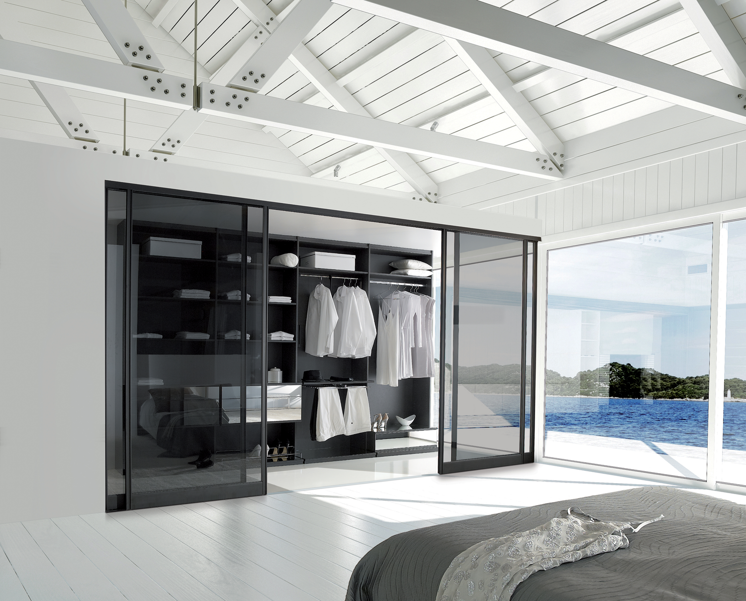 Chambre moderne avec vue sur la mer, armoire ouverte avec vêtements blancs, lit avec literie gris clair, grandes fenêtres laissant entrer la lumière naturelle.