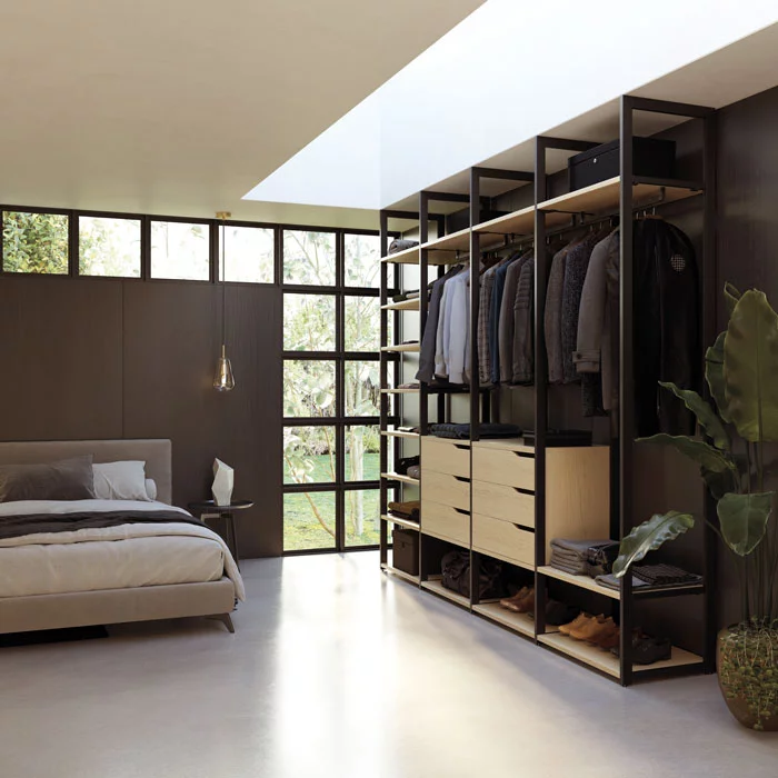 Chambre moderne avec un lit, une grande fenêtre en verre, et une armoire ouverte avec des vêtements suspendus et des tiroirs.