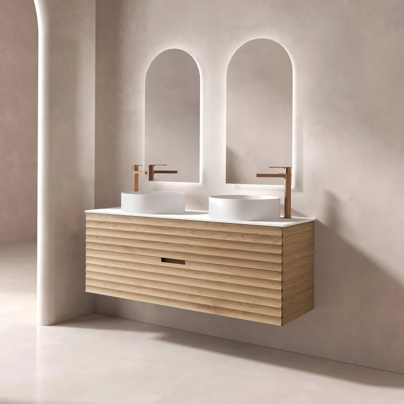 Un meuble de lavabo en bois avec deux vasques blanches et deux miroirs arqués derrière, dans une salle de bain moderne et minimaliste.