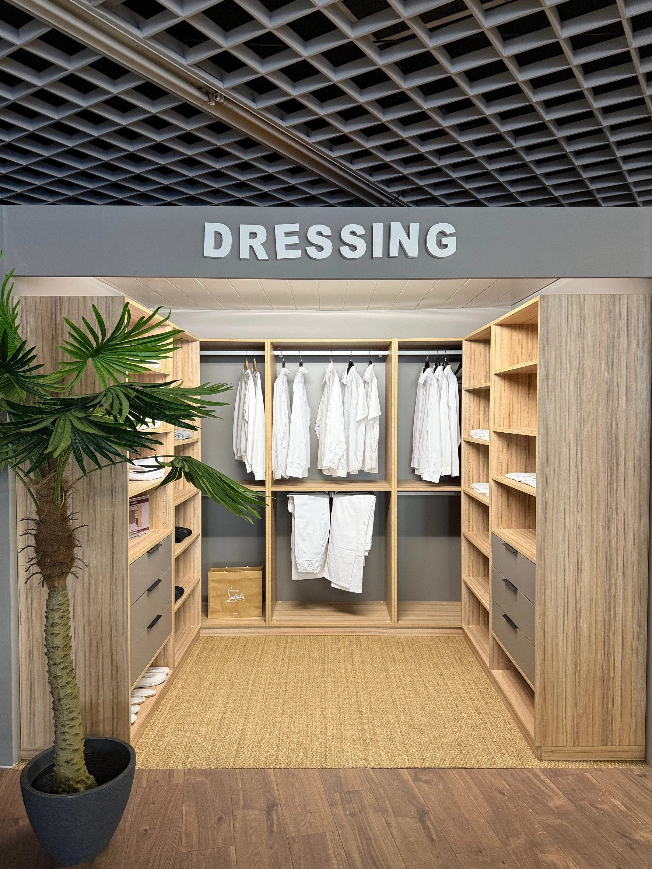 Espace dressing avec penderie de vêtements blancs, étagères en bois, et un tapis beige.