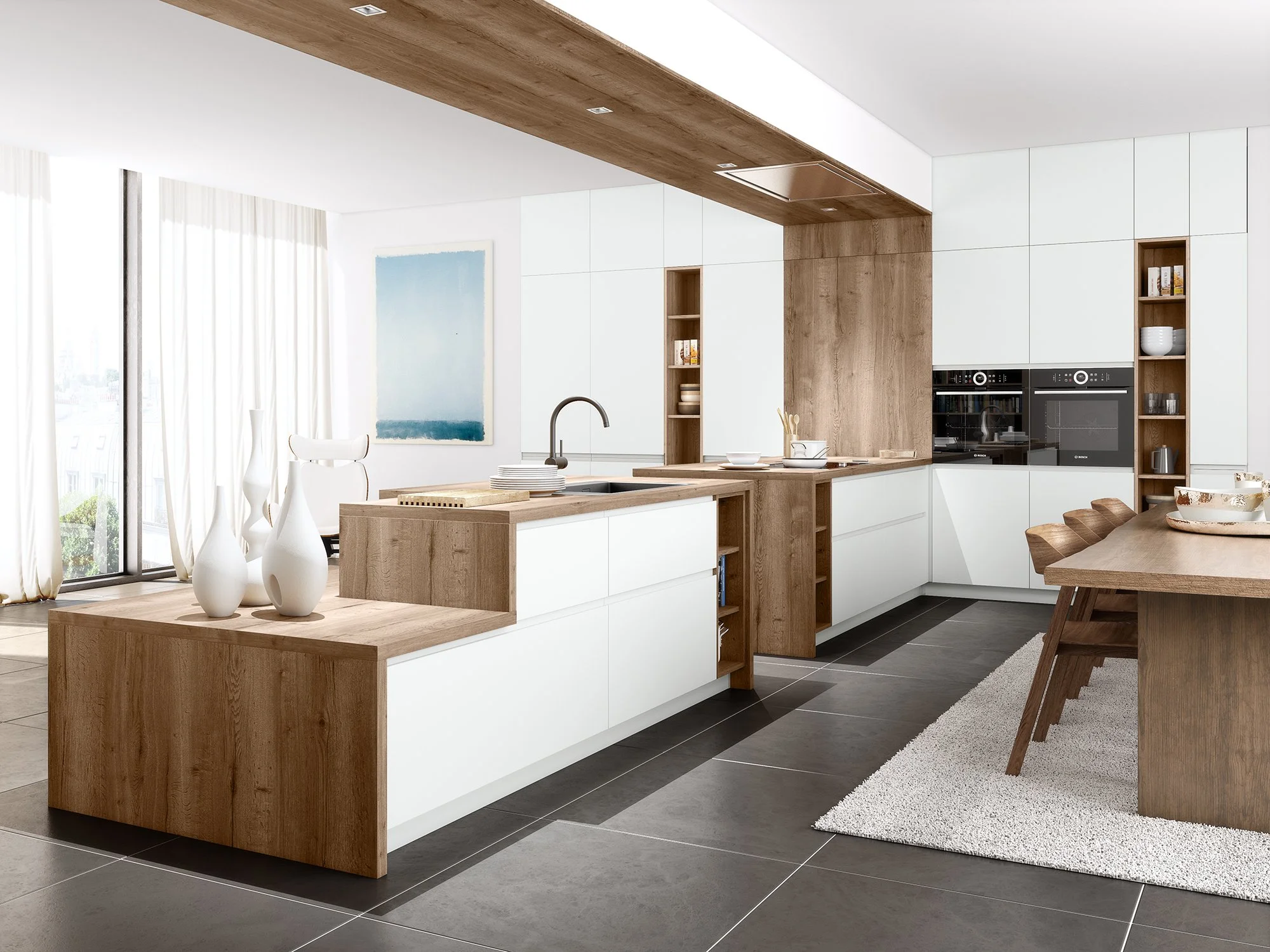 Une cuisine moderne avec des armoires blanches, des accents en bois naturel, un plan de travail en bois, et un espace de repas avec une table en bois et des chaises. Il y a aussi des étagères en bois avec des vaisselle et des livres, et un tableau abstrait blanc et bleu sur le mur.