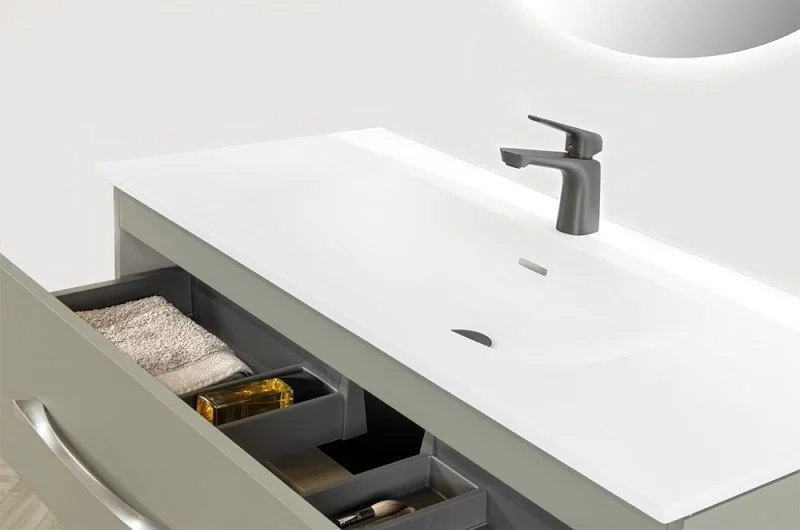 Un meuble-lavabo avec un évier blanc, un robinet noir, et des tiroirs contenant des serviettes, un savon et des produits de toilette.