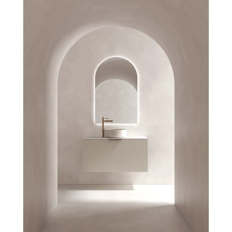 Vue d'une salle de bain minimaliste avec un lavabo rond blanc, un miroir arqué, et un éclairage indirect.