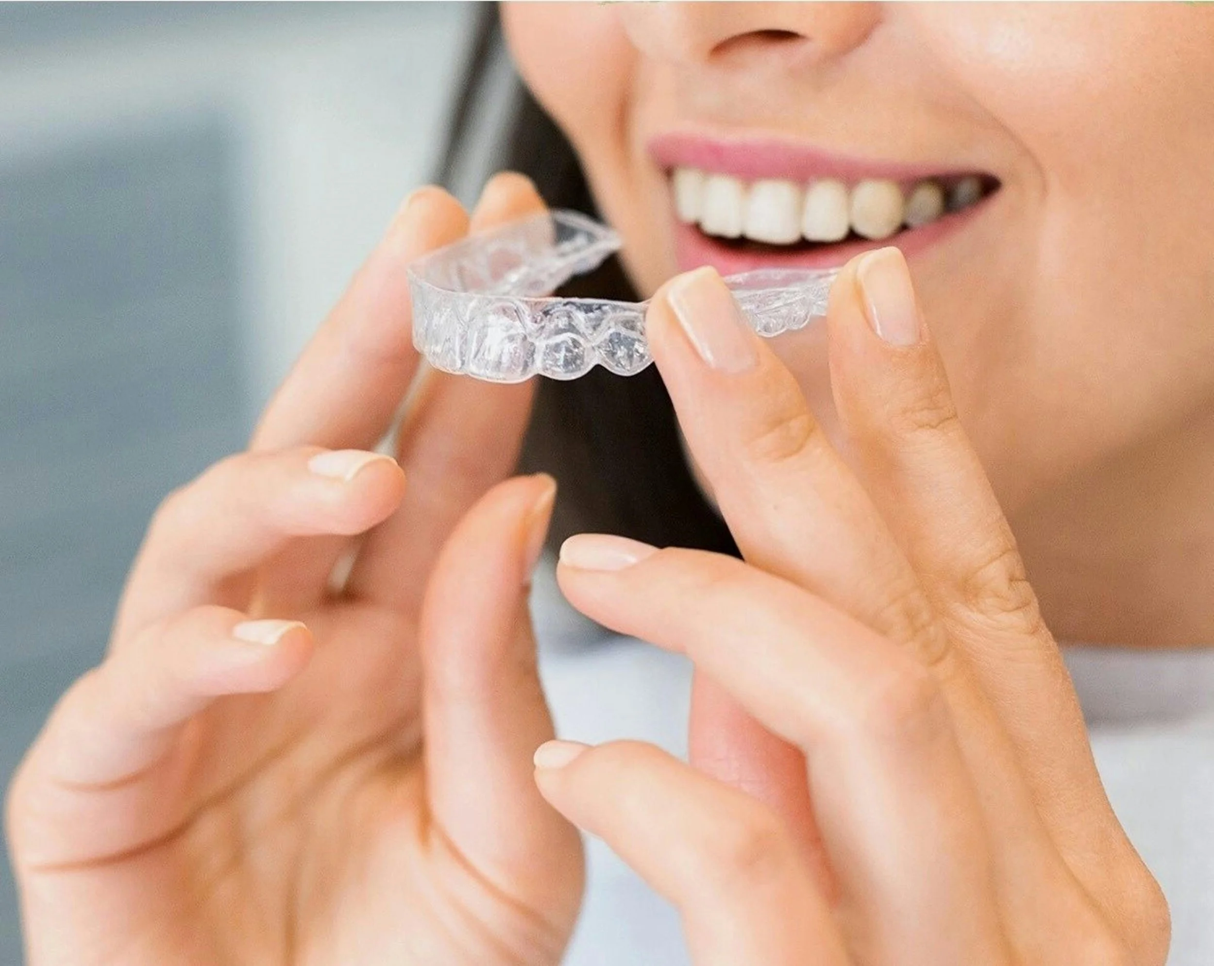 Close-up of a woman smiling and holding a clear dental aligner near her mouth.