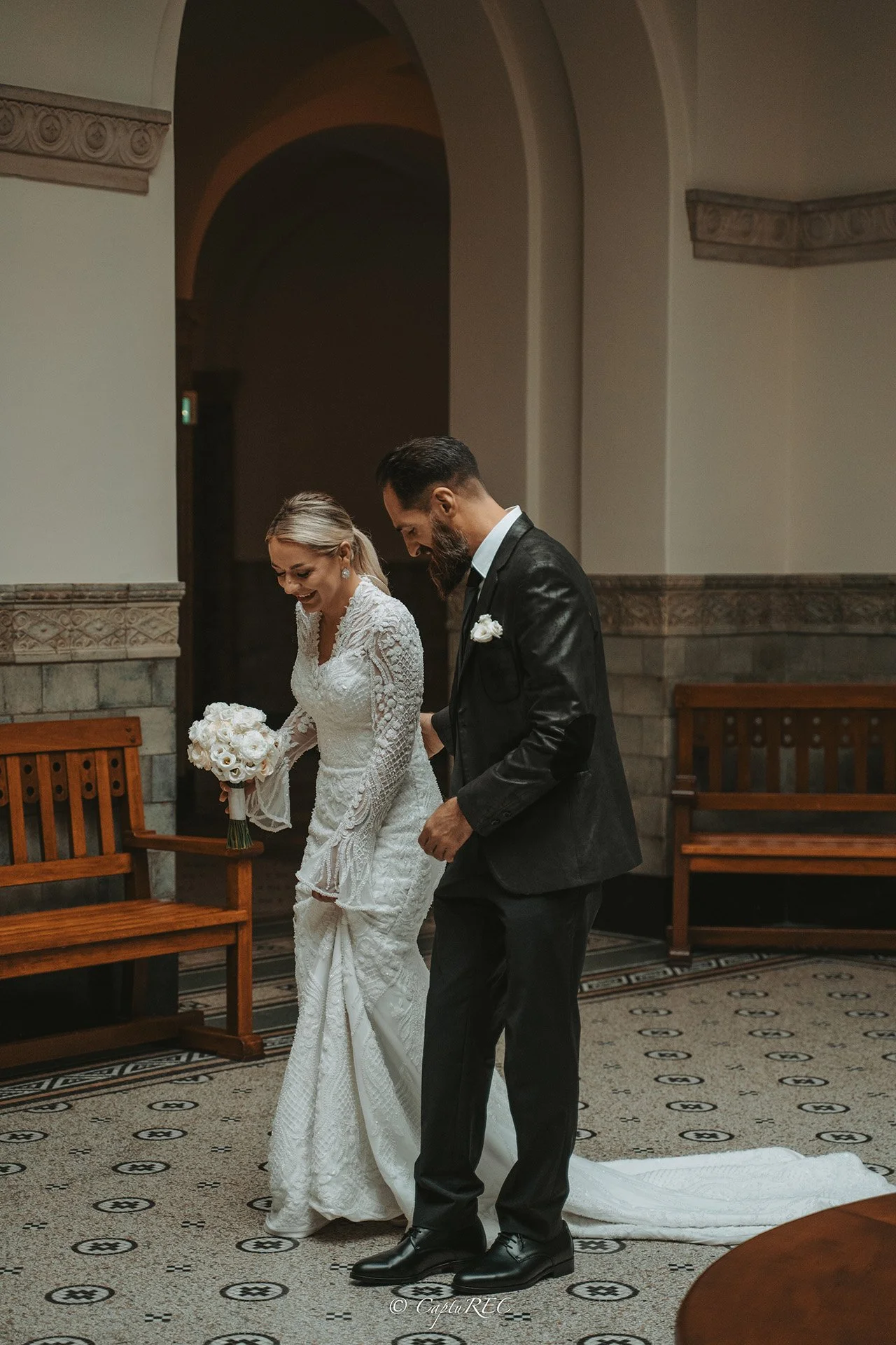 A bride and groom standing together in a church during their wedding ceremony, smiling and holding hands.