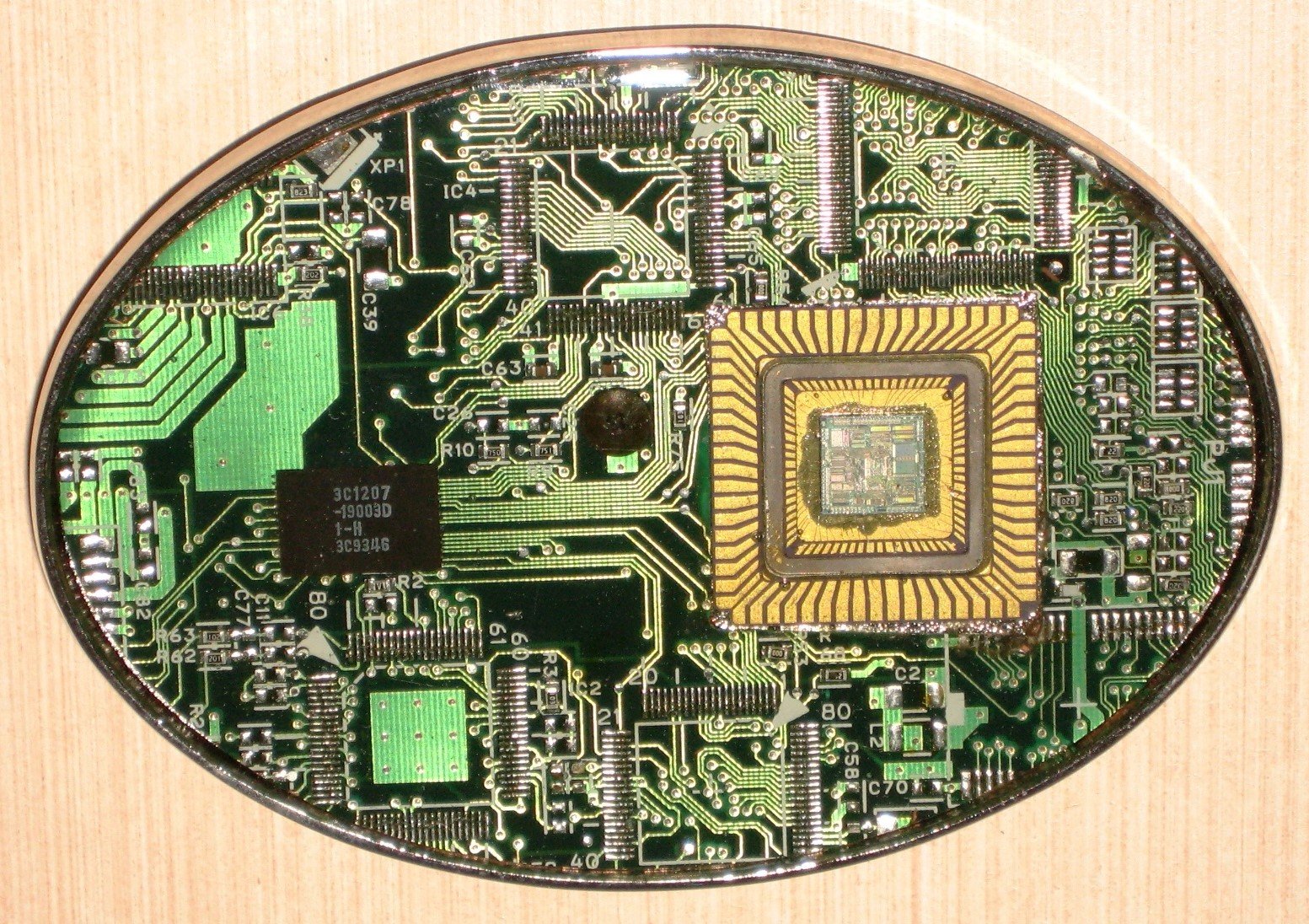 Close-up view of a green printed circuit board (PCB) with various electronic components, including a central square processor, chips, and intricate gold and silver circuitry patterns.