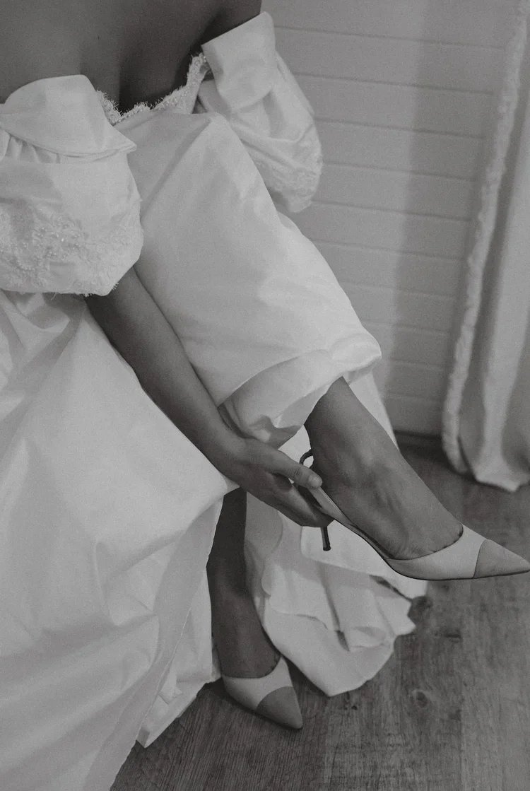 A woman in a wedding dress adjusting her high-heeled shoes.