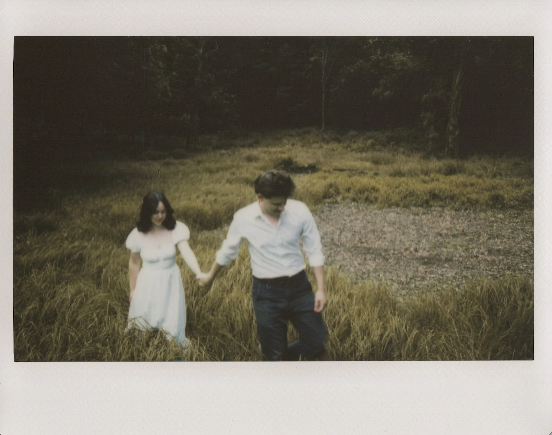 A man and woman holding hands while walking through a grassy field.