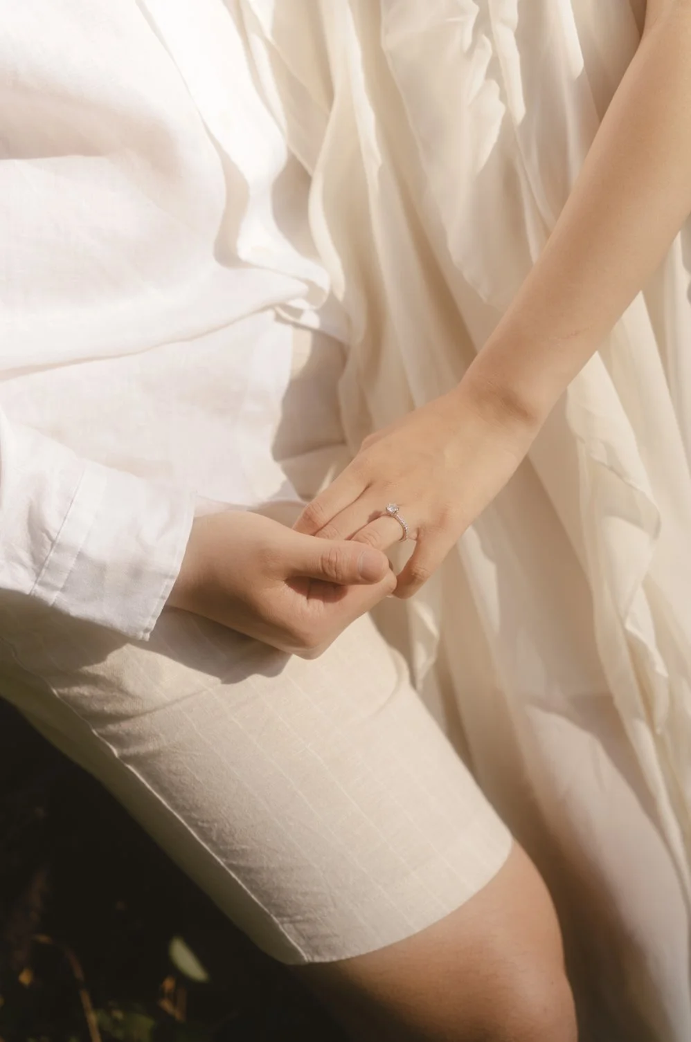 Close-up of a hand holding another hand, with a ring on the finger, against a backdrop of light-colored fabric and clothing.