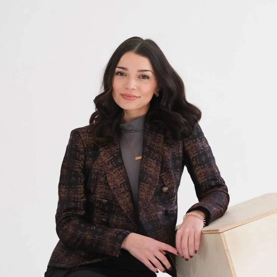 A young woman with long dark wavy hair smiling and posing in front of a colorful background.