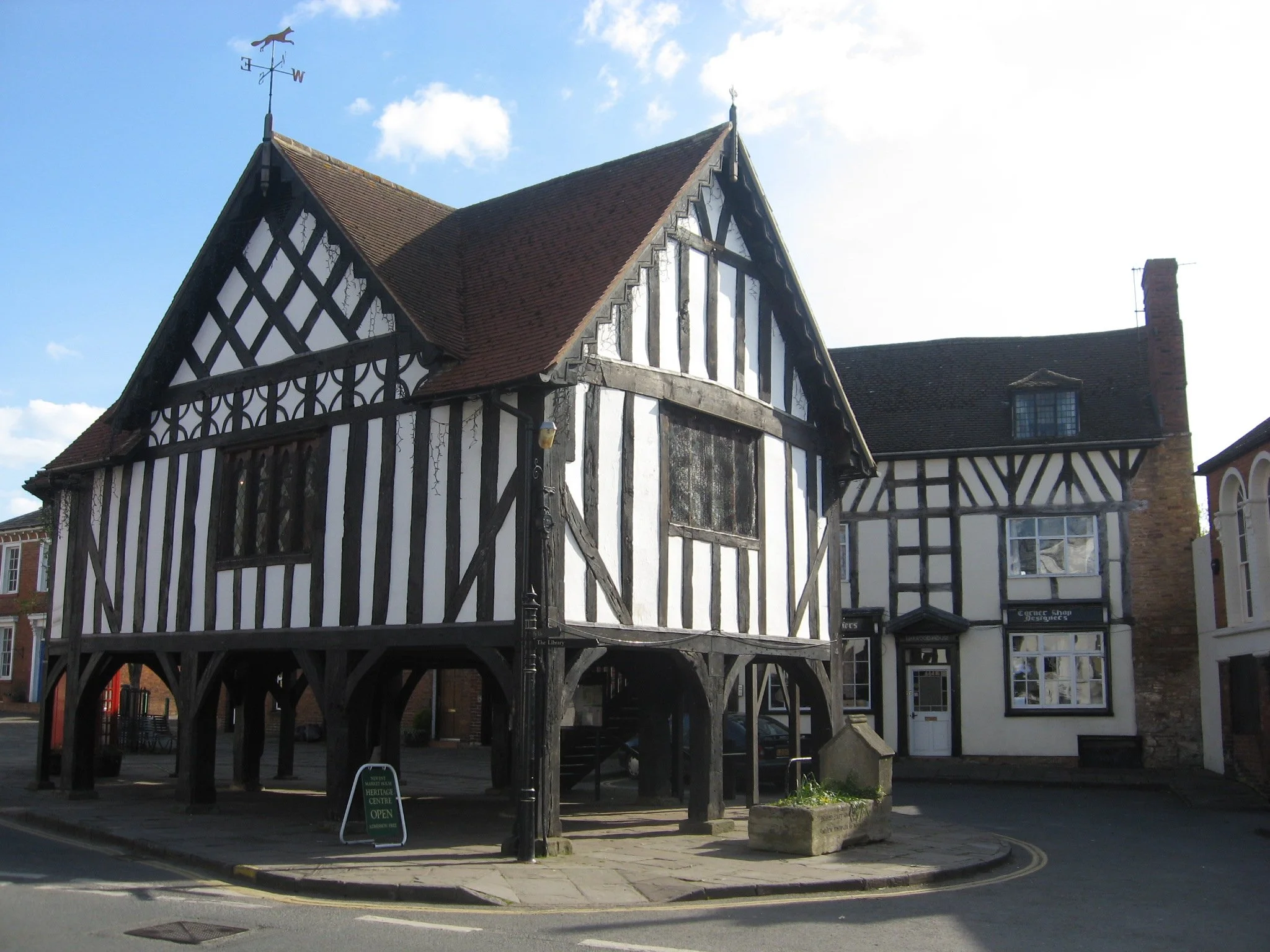 A black and white timber-framed building on a street corner with a red tiled roof and a weather vane on top.