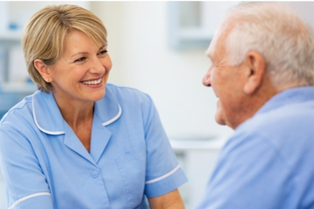 A female nurse smiling and talking to an elderly male patient in a medical setting.