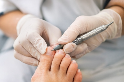 Close-up of a person wearing gloves using a nail drill on a client's toenail.