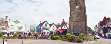 Town square with historic clock tower, shops, and outdoor seating in a coastal town.
