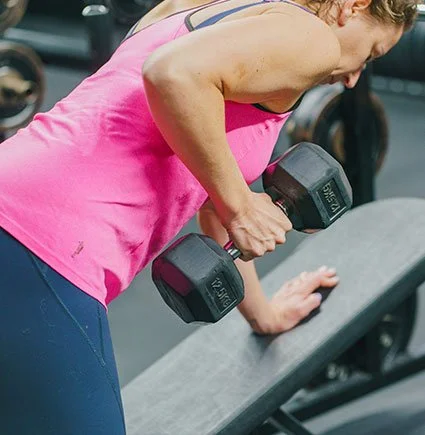 A woman in pink workout clothes lifting a dumbbell in a gym.