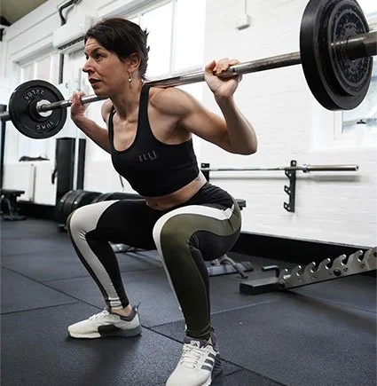 Woman performing a barbell squat in a gym.
