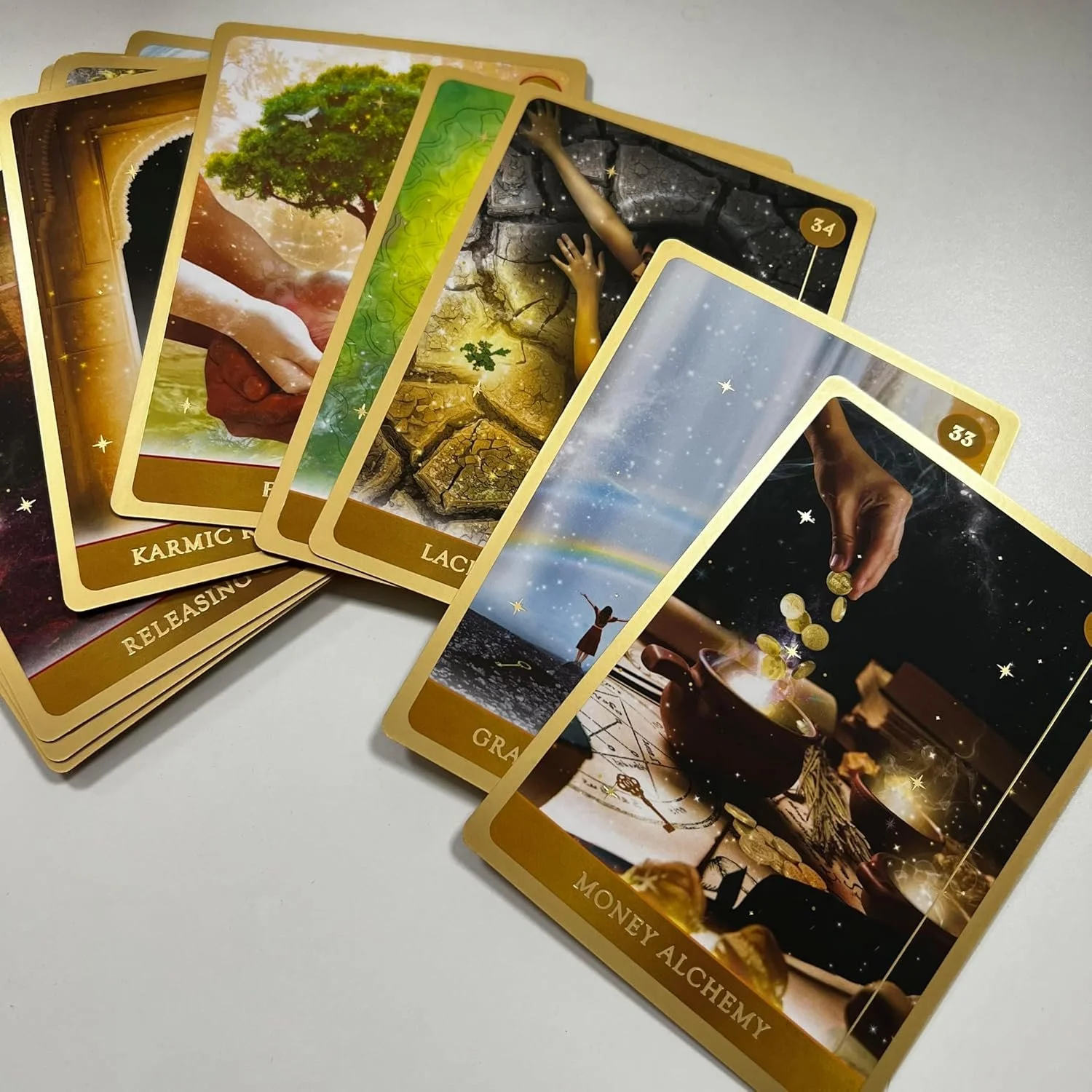 A spread of fantasy and mystical themed tarot or oracle cards, including images of a tree, hands reaching from cracked earth, a person with outstretched arms under the sky, and a hand pouring coins into a bowl, with labels like 'Karmic Release,' 'Lac