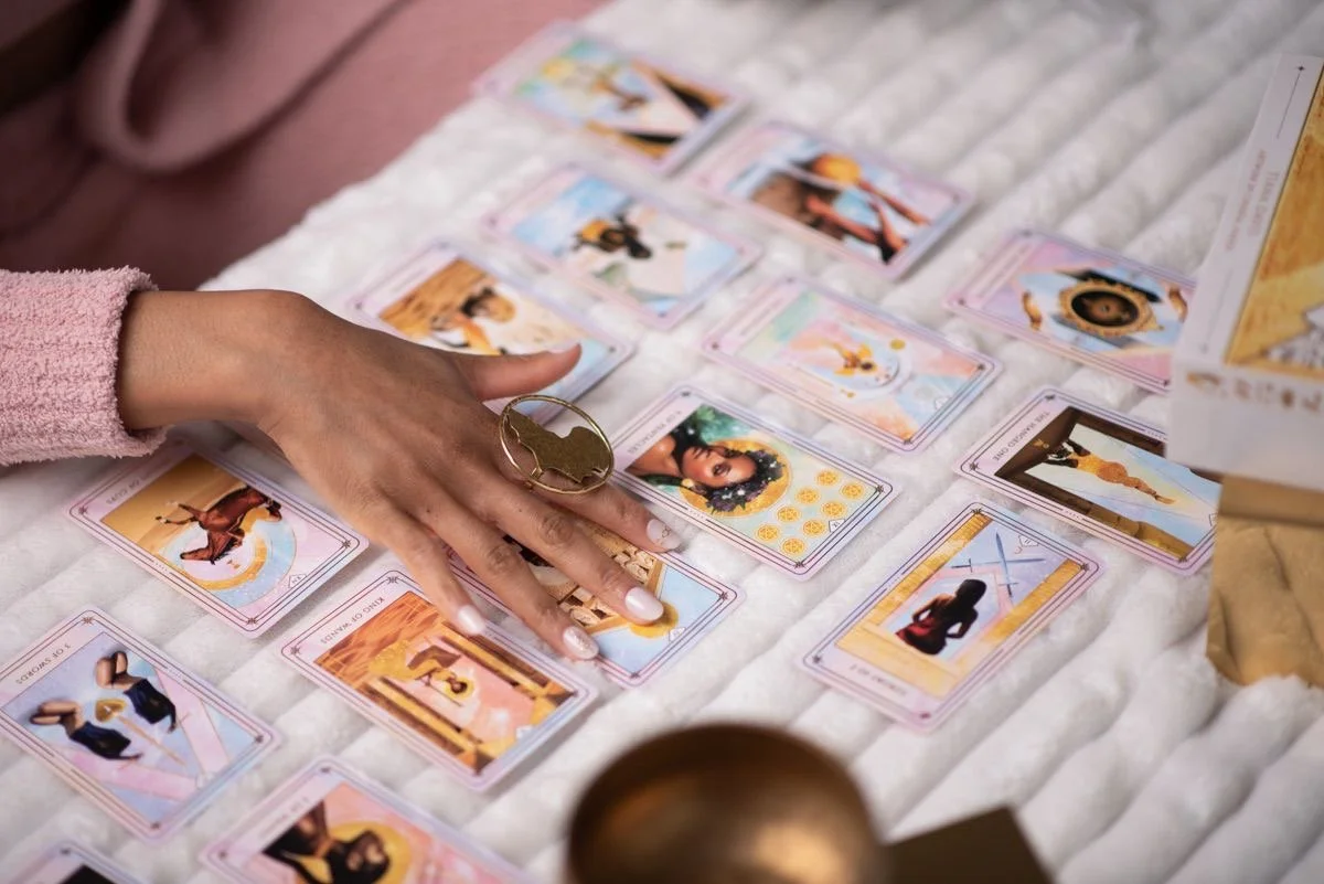 A person browsing through a spread of tarot or oracle cards laid out on a white textured surface, with various illustrated cards visible.