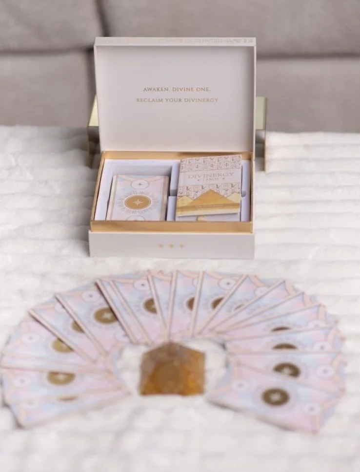 Open card deck box with gold accents and cards inside, placed on a white surface, with fan-shaped currency notes arranged in a semi-circle in front.