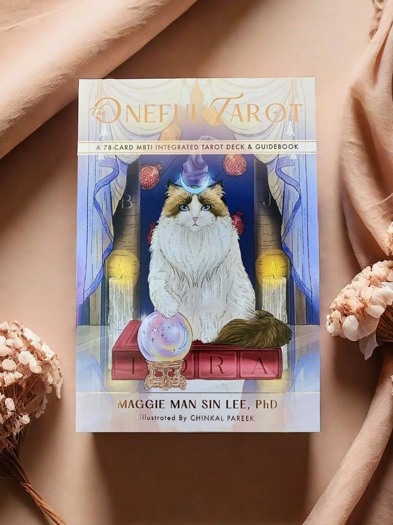 Book titled "The Neon Tarot" featuring an illustrated cat with blue eyes sitting in front of candlelights, drapes, and a crystal ball with the word "VIRA" on the cover.