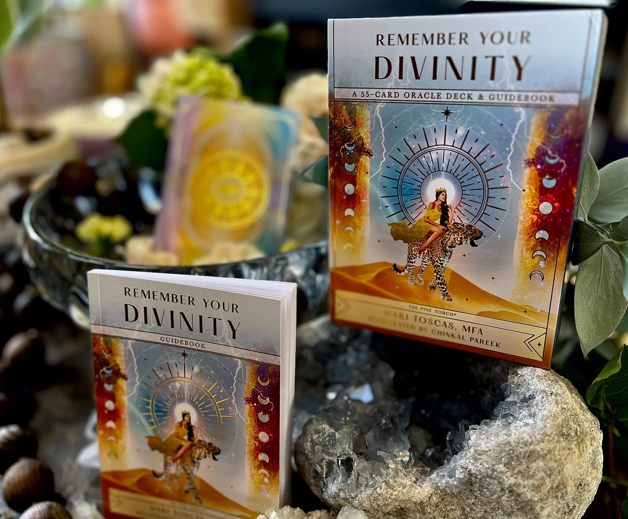 Cards with the title 'Remember Your Divinity' displayed on a crystal and surrounded by greenery and decorative items.