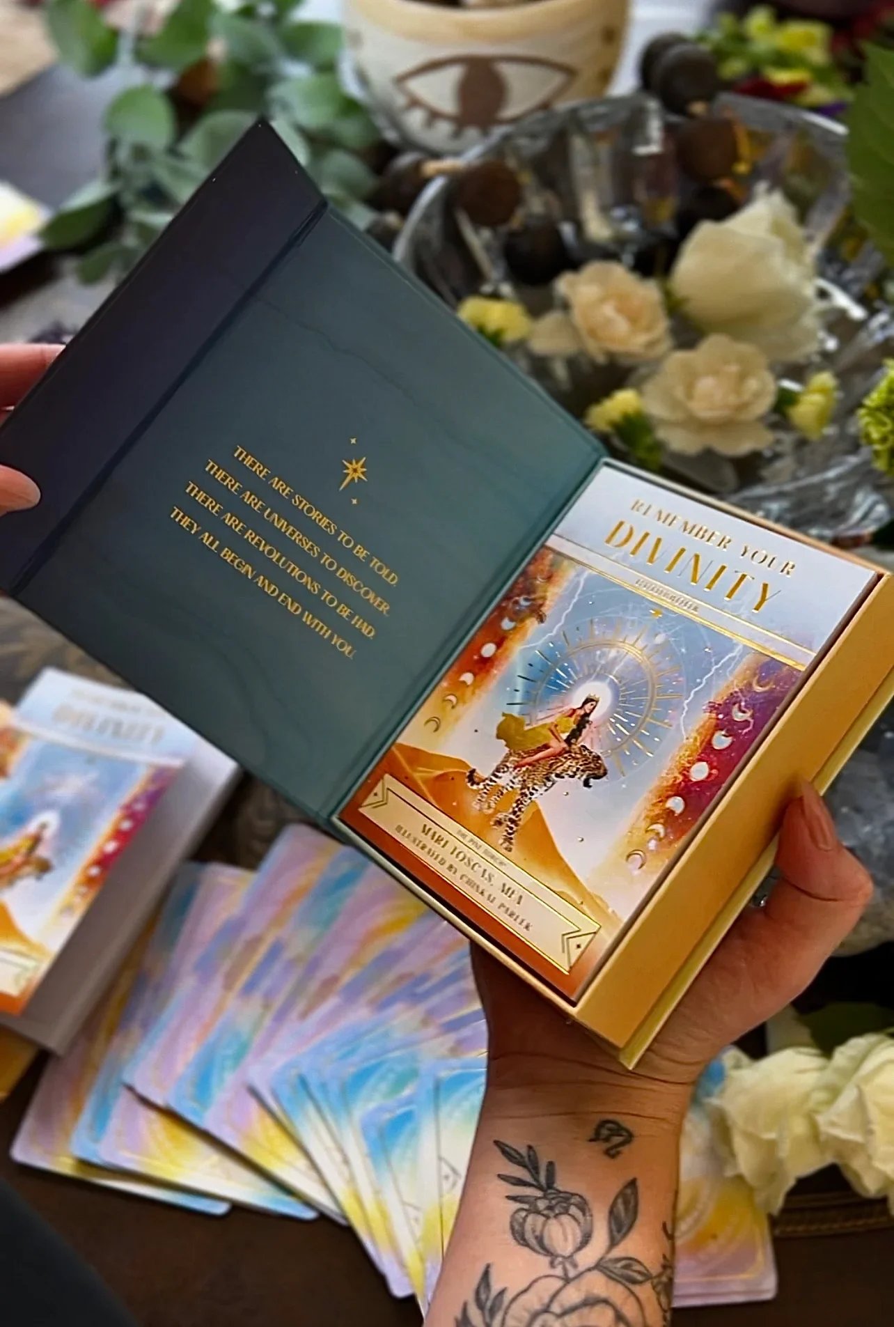 Person holding an open book titled 'We Are Merging Your Destiny'. The left page contains a quote about stories and universes, and the right page features a colorful illustration of a woman riding a tiger, surrounded by celestial symbols and patterns.