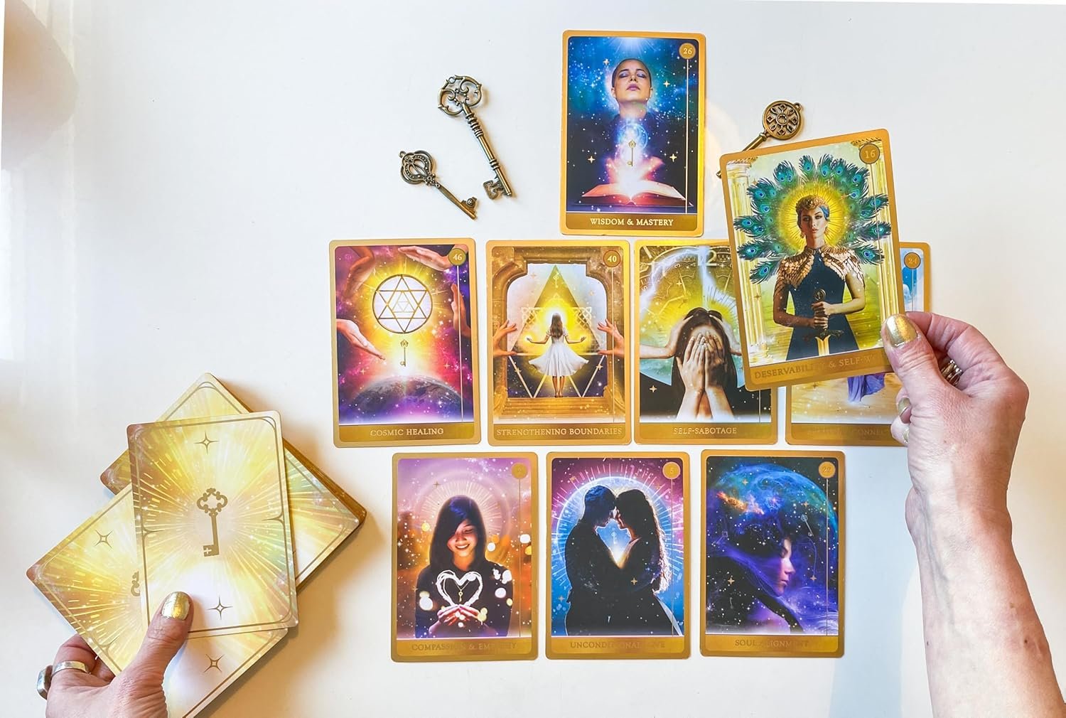 Person holding a card with a peacock on it, surrounded by various Tarot and oracle cards on a white table, with two keys above.