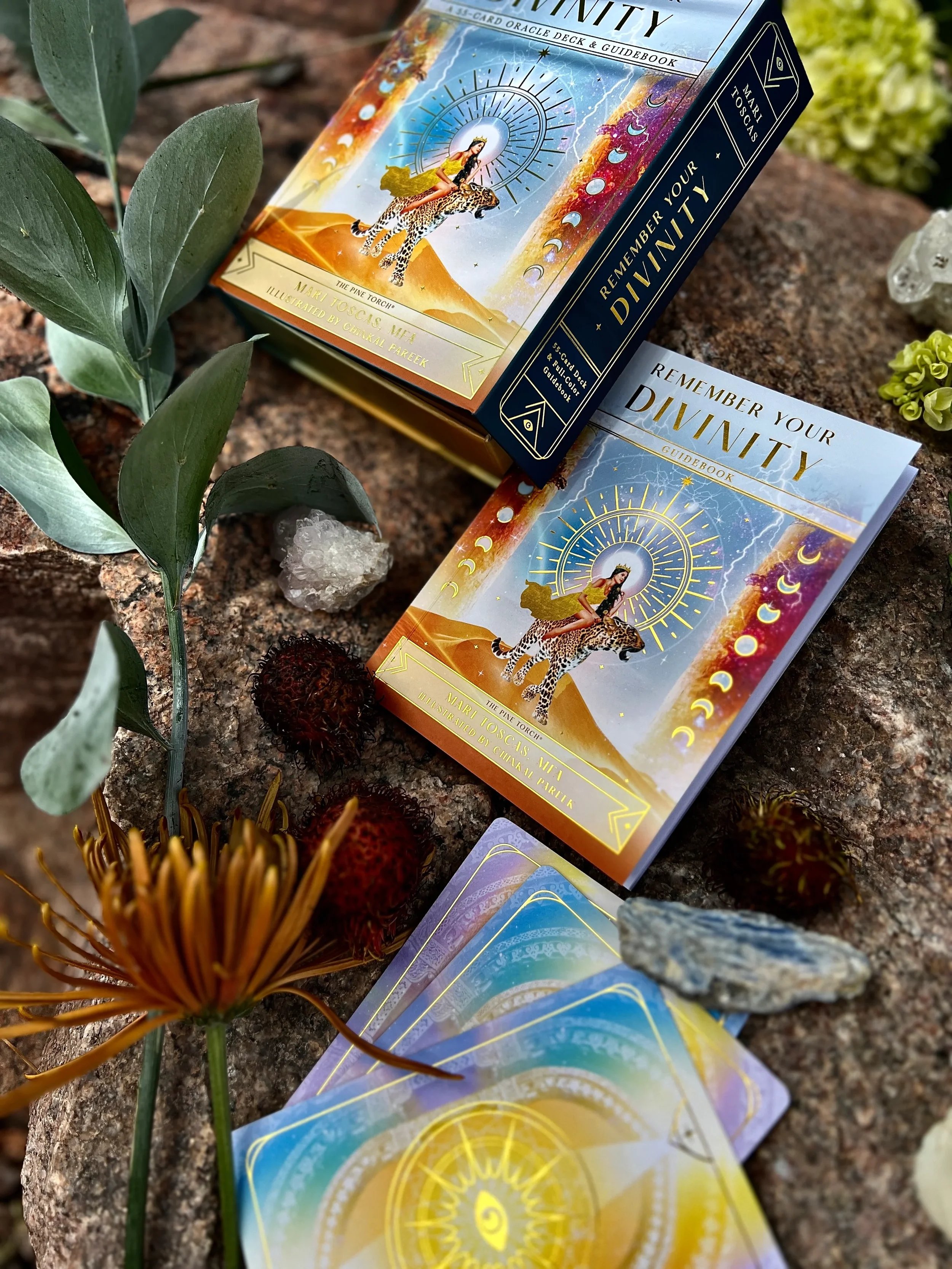 A deck of tarot or oracle cards titled "Remember Your Divinity" with an illustrated woman riding a leopard, set on a rocky surface surrounded by plants, stones, and flowers.