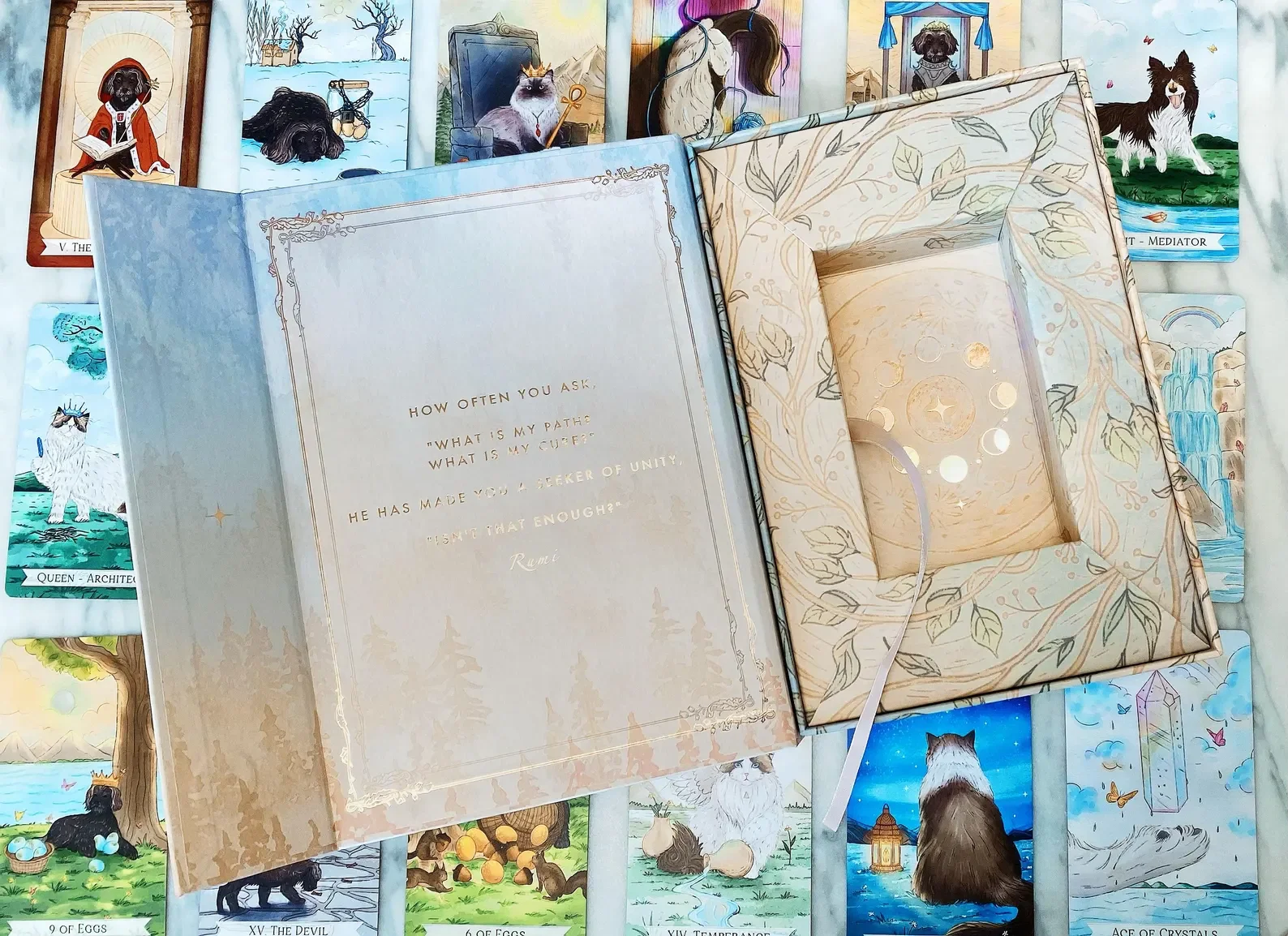 Open card with a quote from Rumi and a lit candle inside, surrounded by tarot cards featuring animals on a white surface.