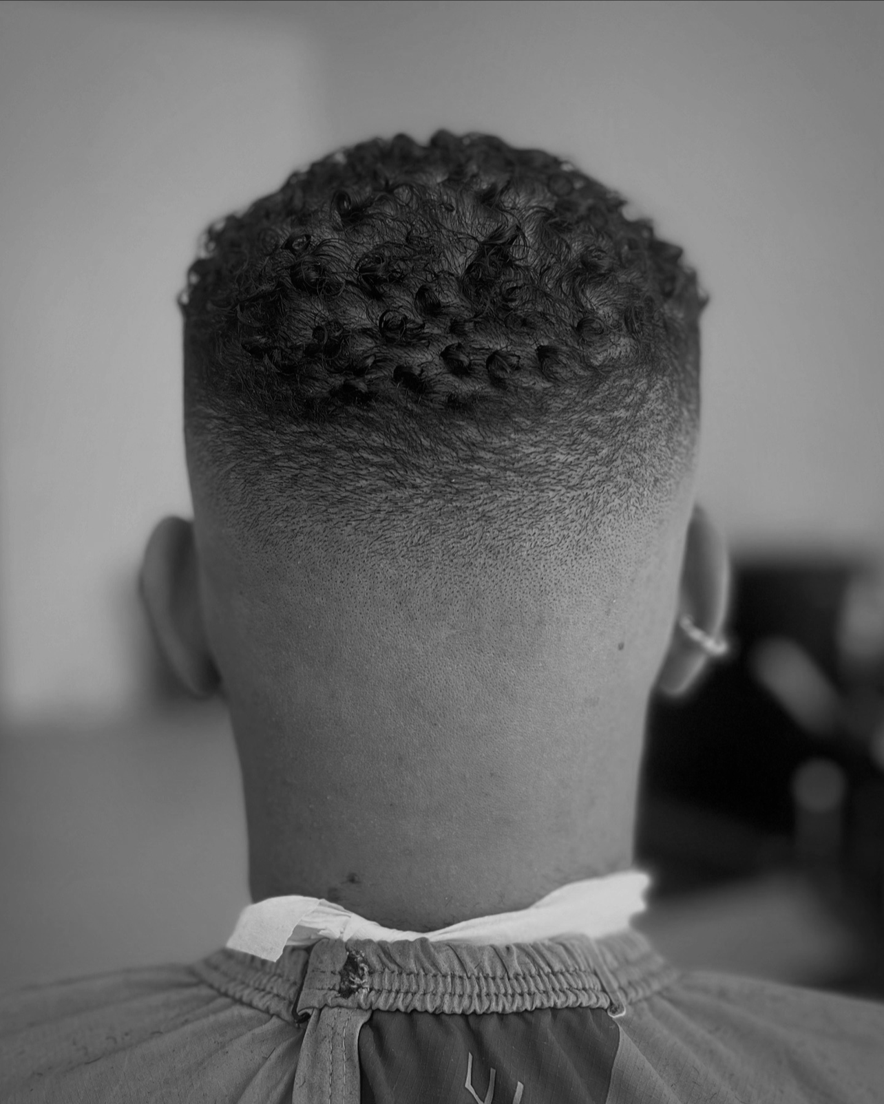 Back of a person's head with a short, curly hairstyle and a fade haircut, wearing a sports jersey.