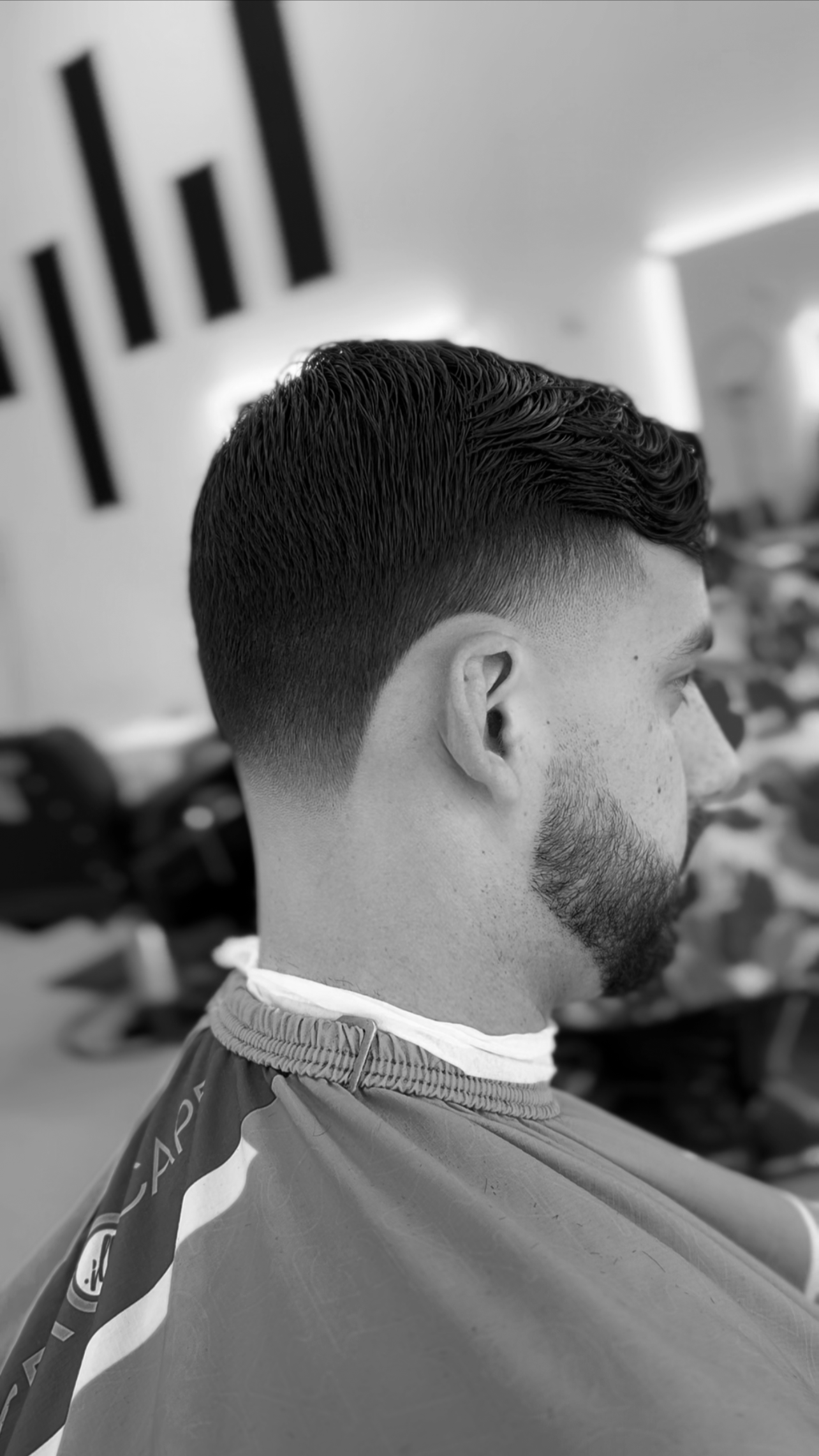 A man with a fresh, styled haircut sitting in a barber shop with a barber cape.