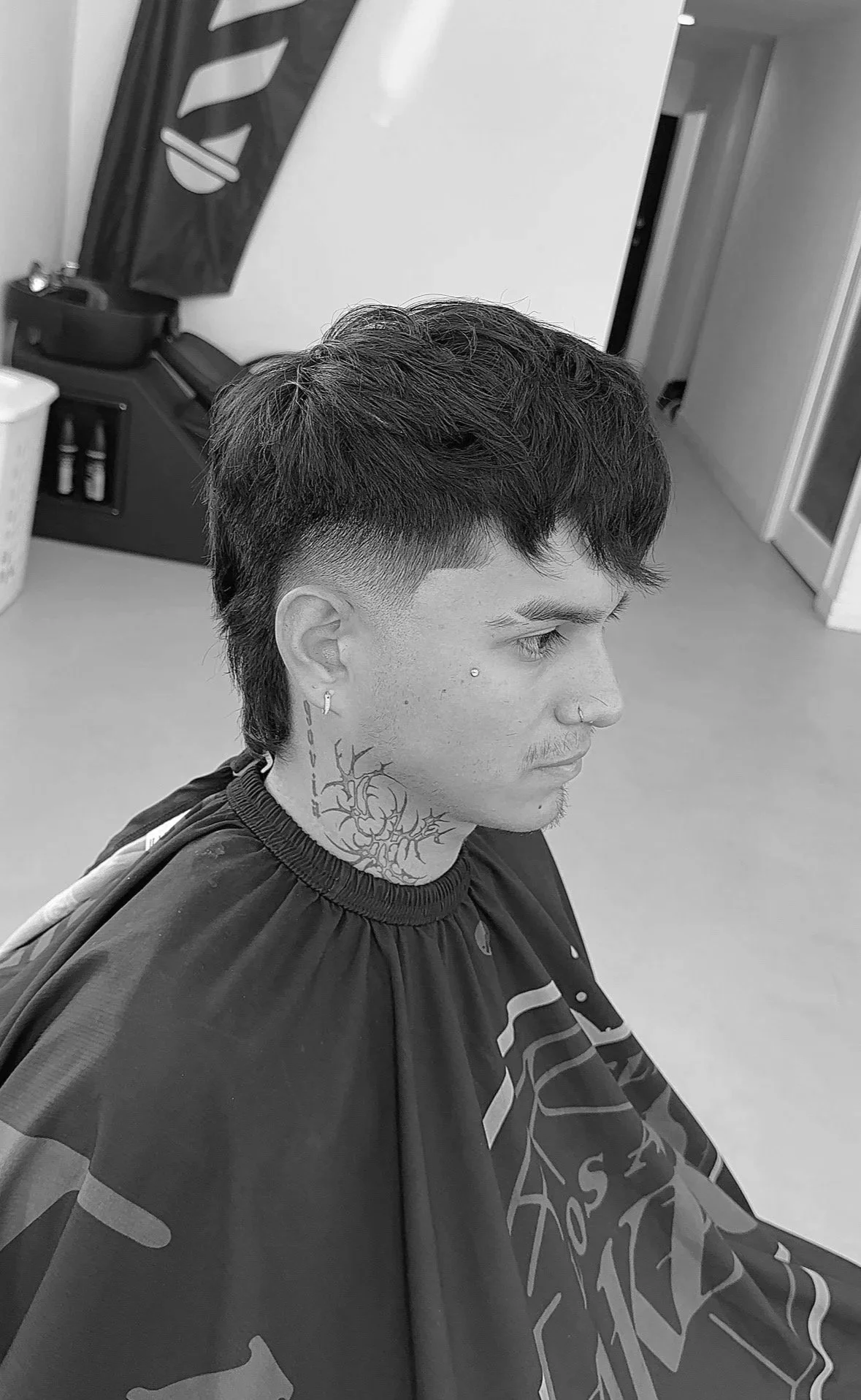 Young man with a short, textured hairstyle and tattoos, sitting in a salon chair.