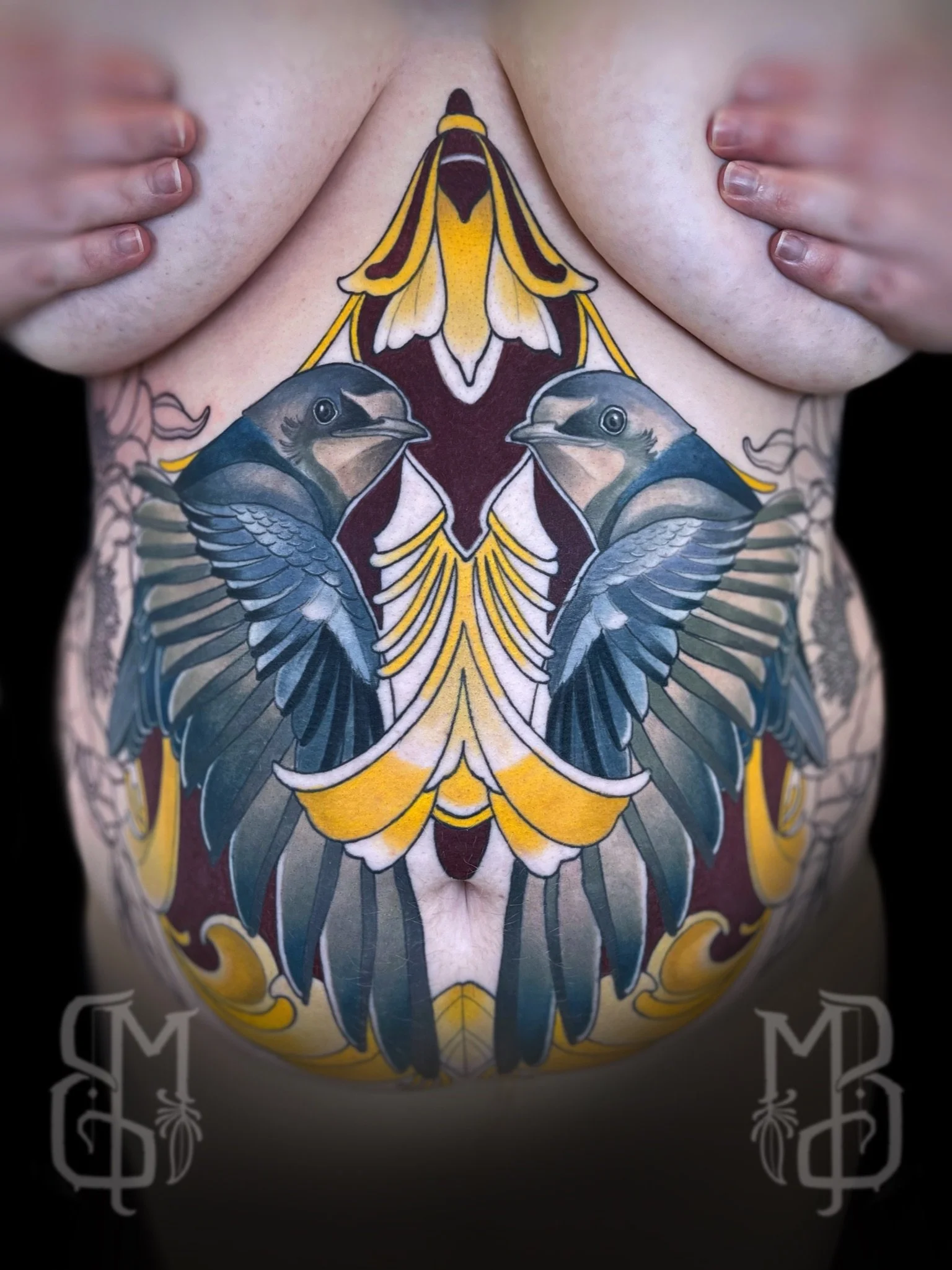Colorful tattoo of a symmetrical design on the torso of a woman, featuring two birds, with ornamental work to enchant the body’s figure