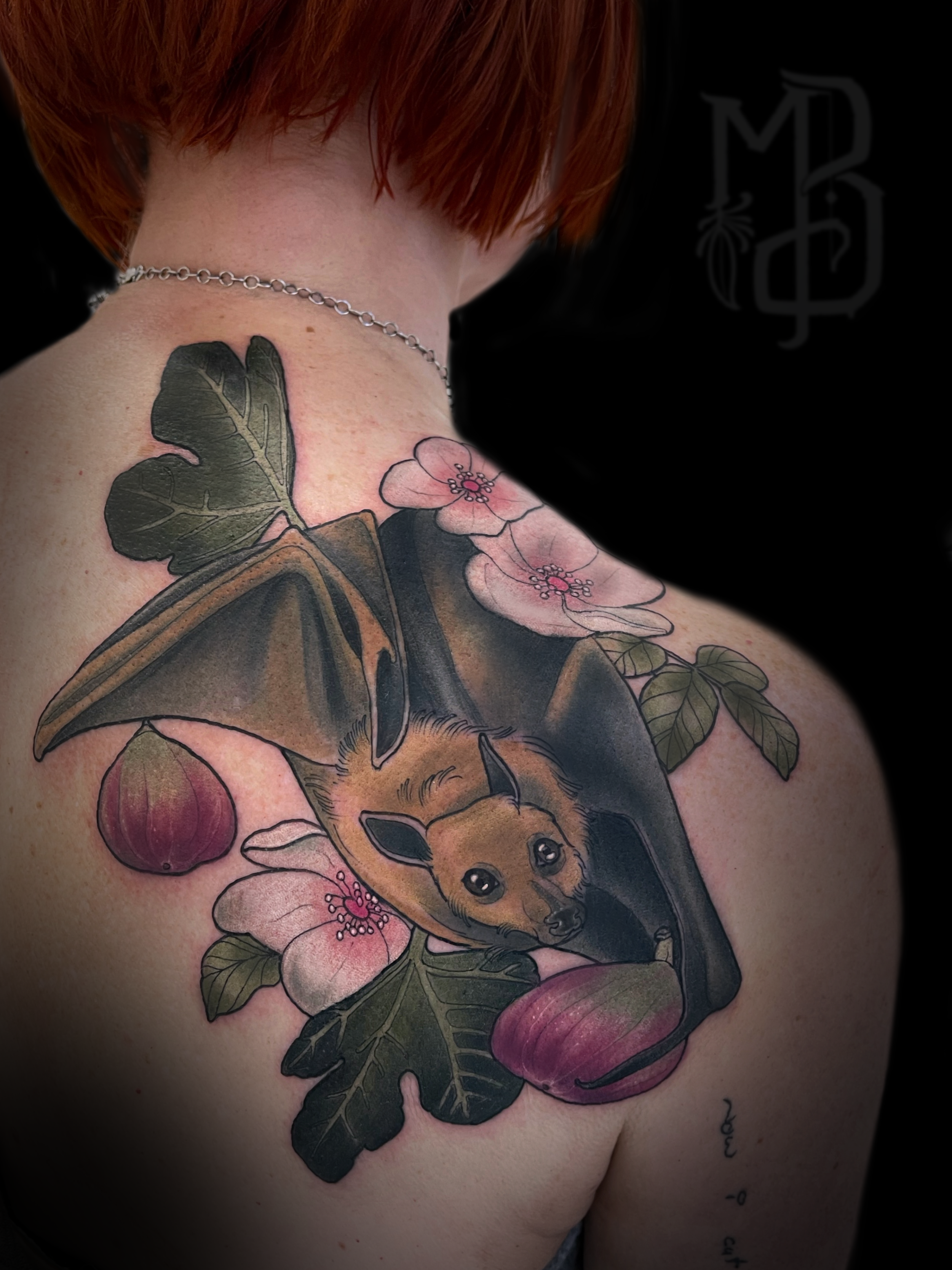 Colorful tattoo of a bat with pink flower and figs in Neotraditional style on the person's shoulder and upper chest.