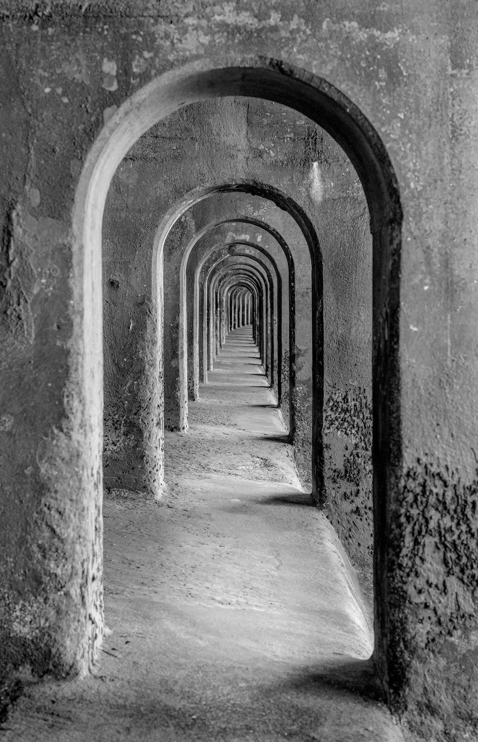 Black and white photo of a repeated series of arched doorways or windows creating a tunnel effect.