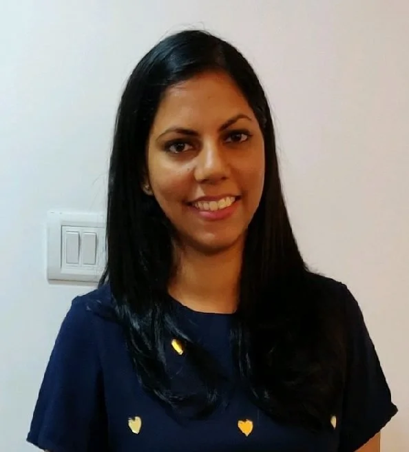 Close-up of a young Asian woman with shoulder-length black hair, smiling broadly, surrounded by green foliage.