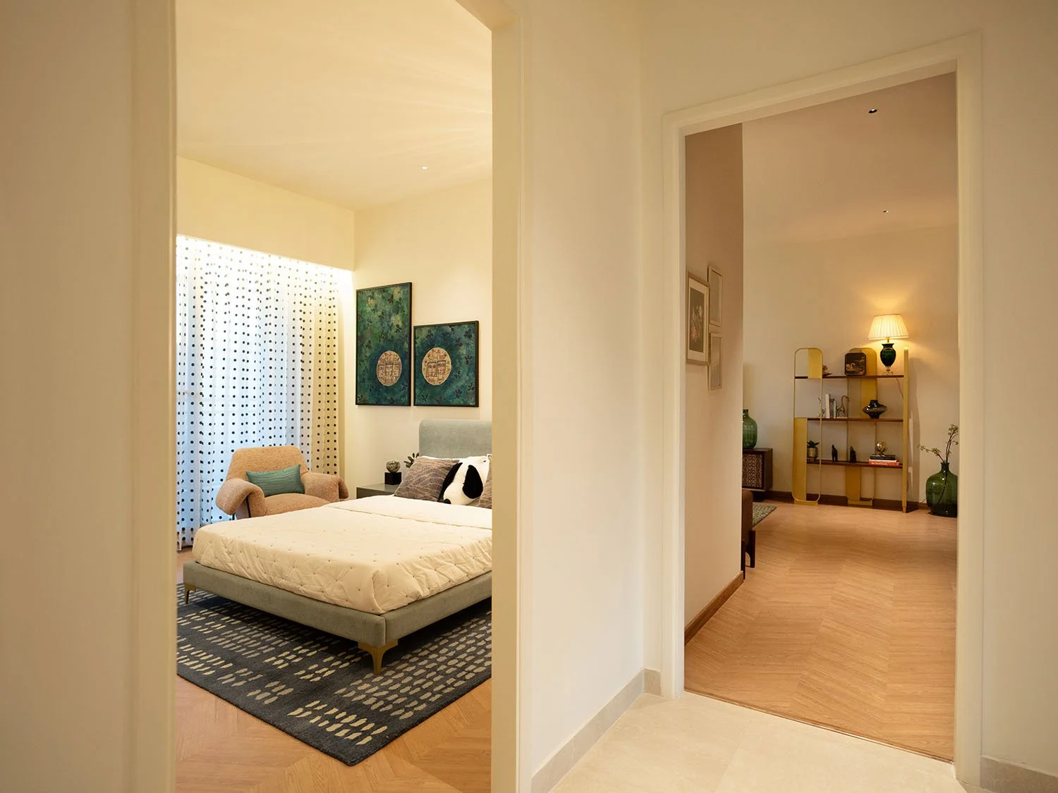 View of a bedroom with a bed, an armchair, wall art, and a curtain in the background, seen through doorways.